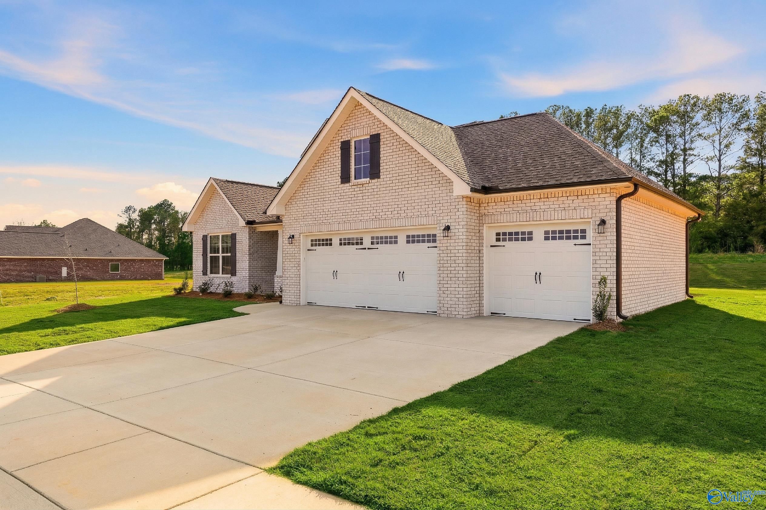 Brick 1.5-story home with 3-car garage, driveway, and lush green lawn in Cain Park, Hartselle, Alabama - Davidson Homes The Rockford