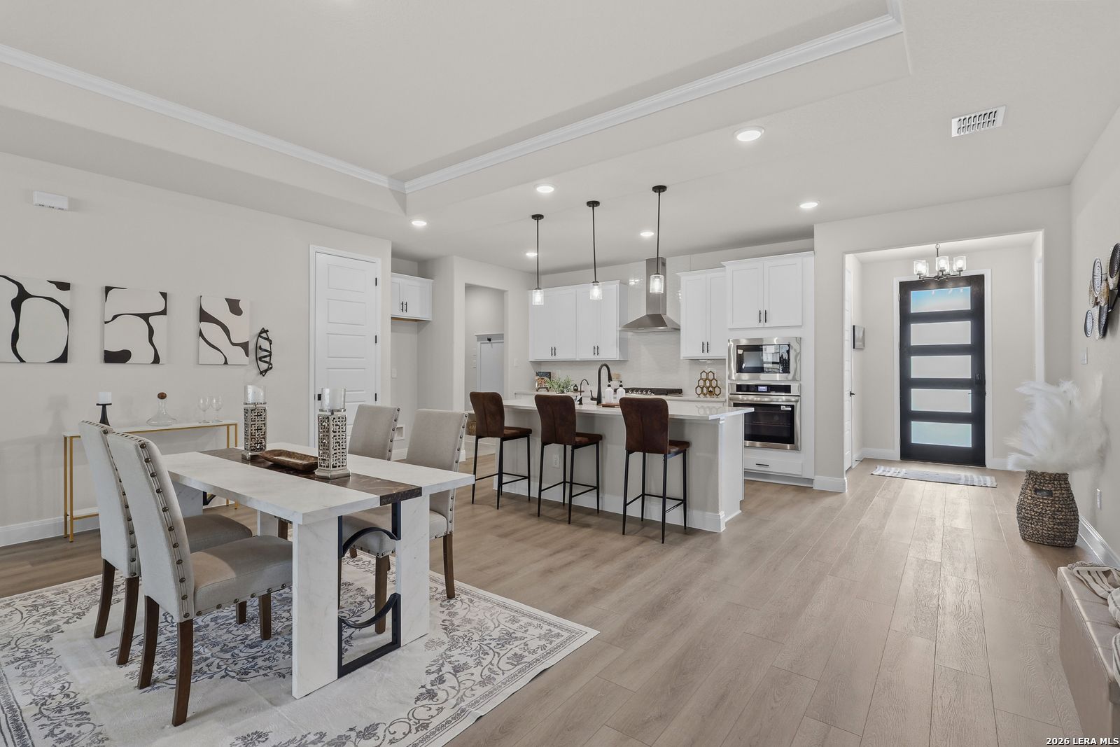 Open-concept kitchen and dining area with white cabinets, stainless appliances, bar island, and light wood floors in The Lanier G, Castroville, Texas