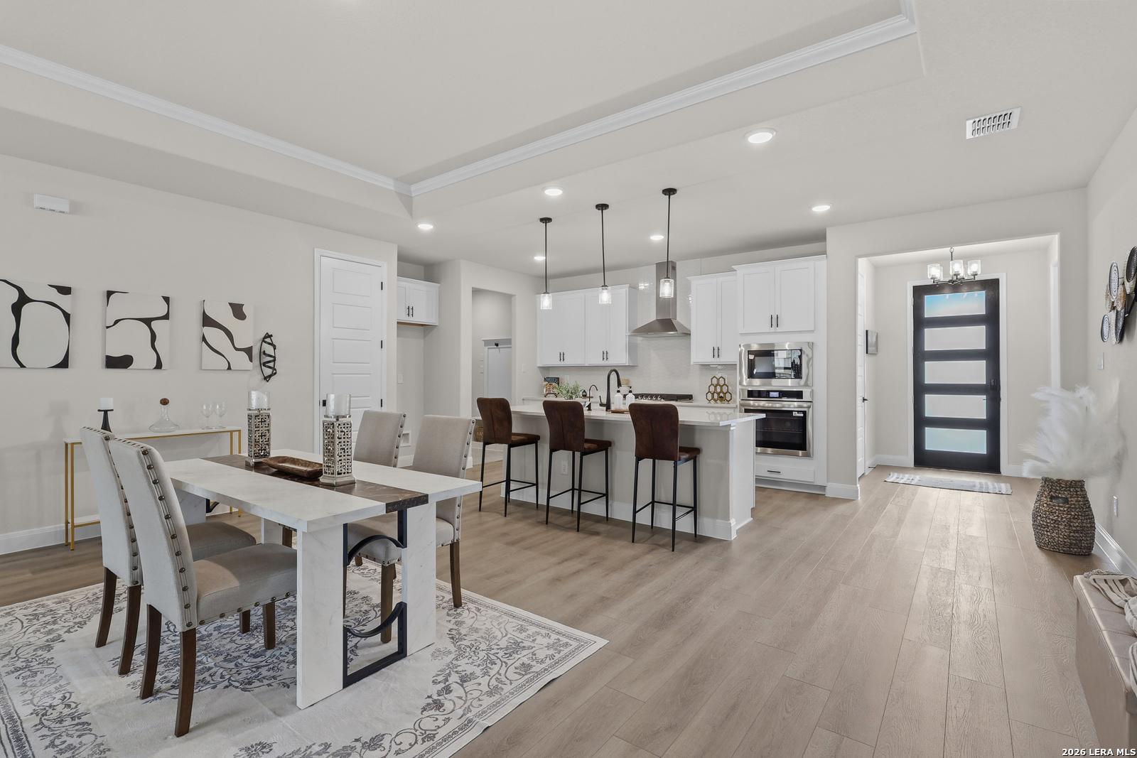 Open-concept kitchen and dining area with white cabinets, stainless appliances, bar island, and light wood floors in The Lanier G, Castroville, Texas