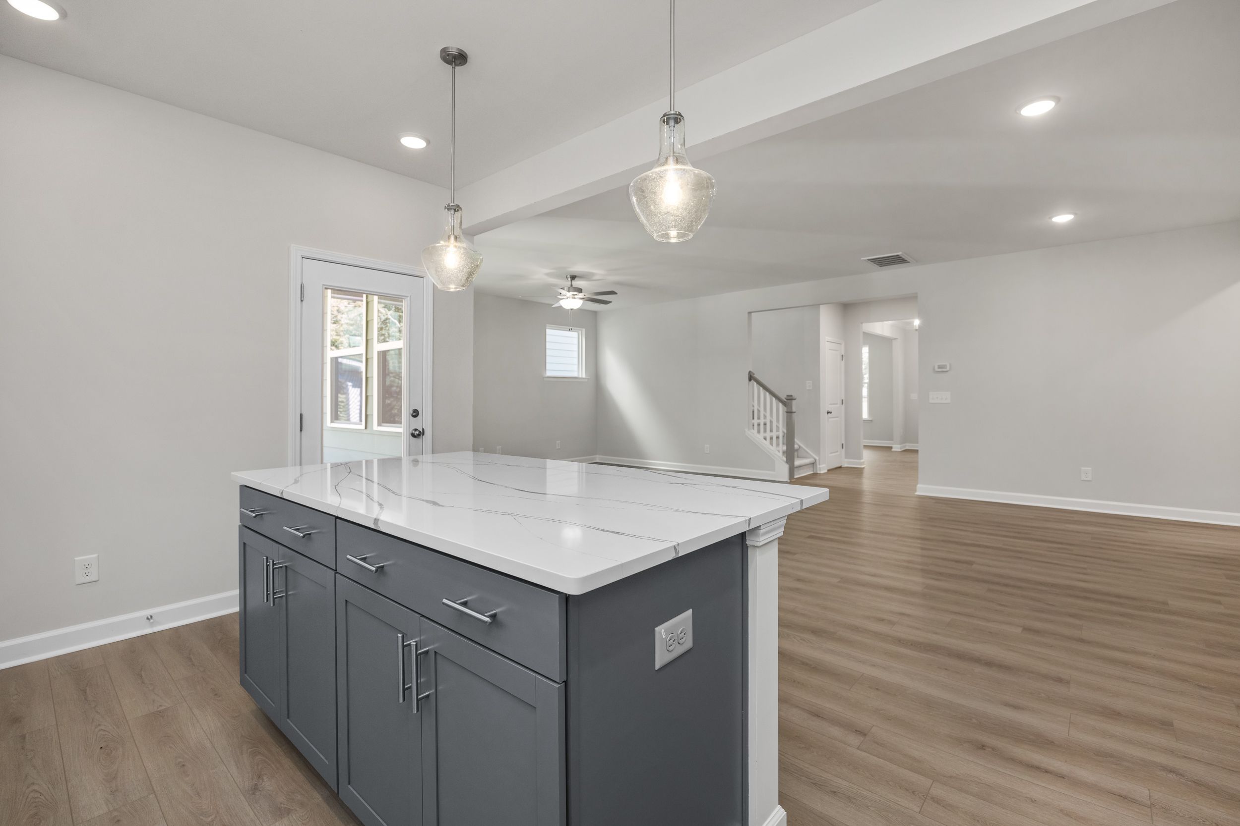 Modern kitchen island in The Aspen C with white quartz top, gray cabinets, pendant lights, open to living area and stairs