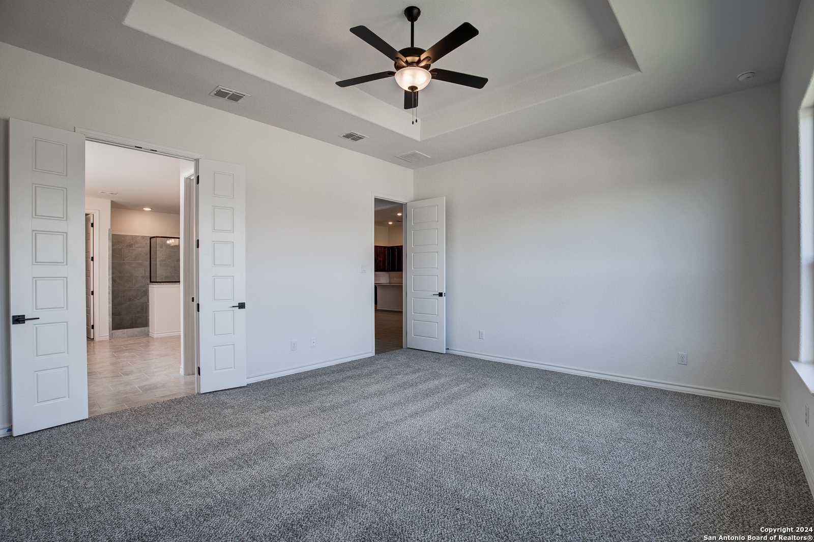 Spacious carpeted master bedroom with ceiling fan and open doors to stone-tiled en-suite bath in Davidson Homes Garner B, Castroville TX