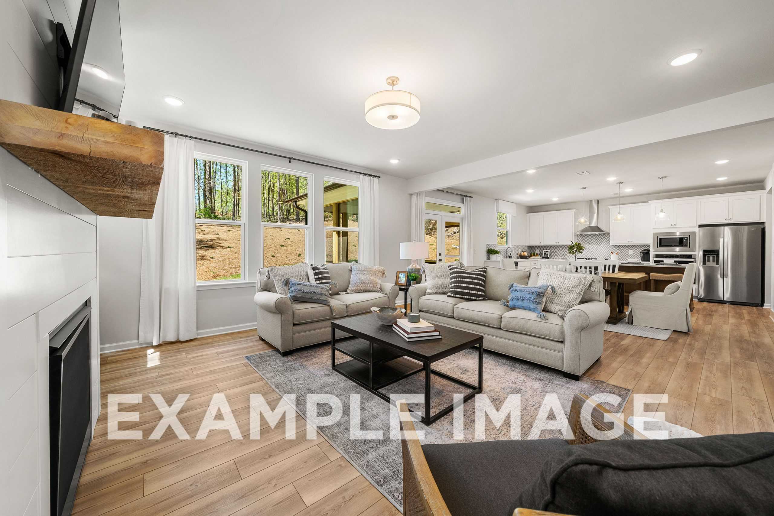 Spacious open-concept living room in The Hickory A featuring wood mantel fireplace, beige sofas, large windows, and white kitchen island