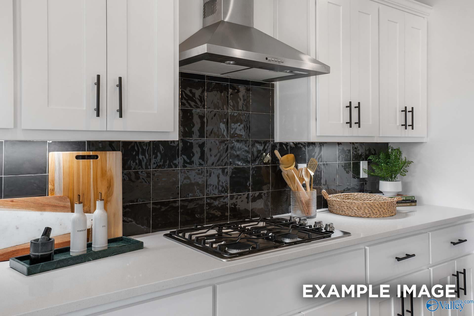 Modern kitchen featuring white shaker cabinets, glossy black subway tile backsplash, and stainless steel range hood in Davidson Homes The Rockford B, Madison, Alabama
