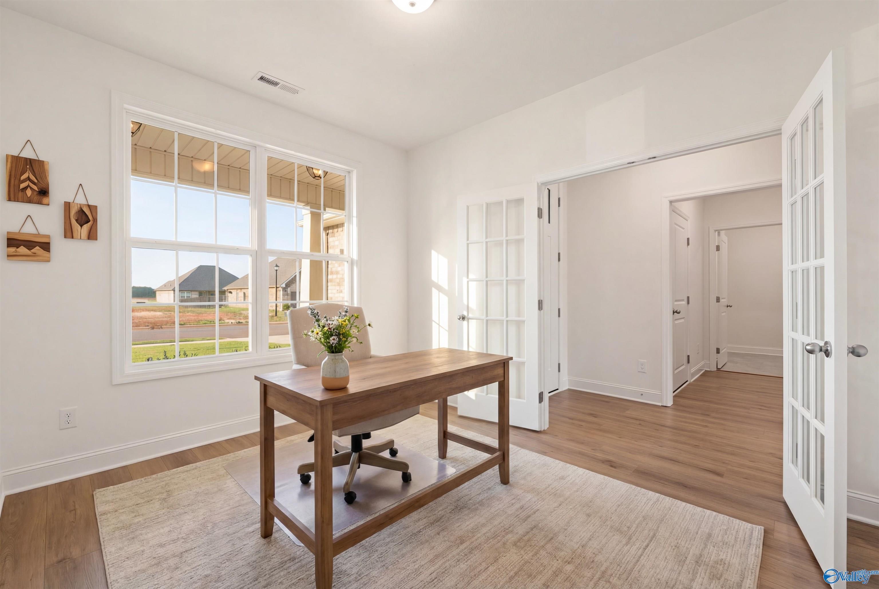 Bright home office with wooden desk, vase of flowers, large windows to fields, and French doors in The Rockford B, Toney, AL