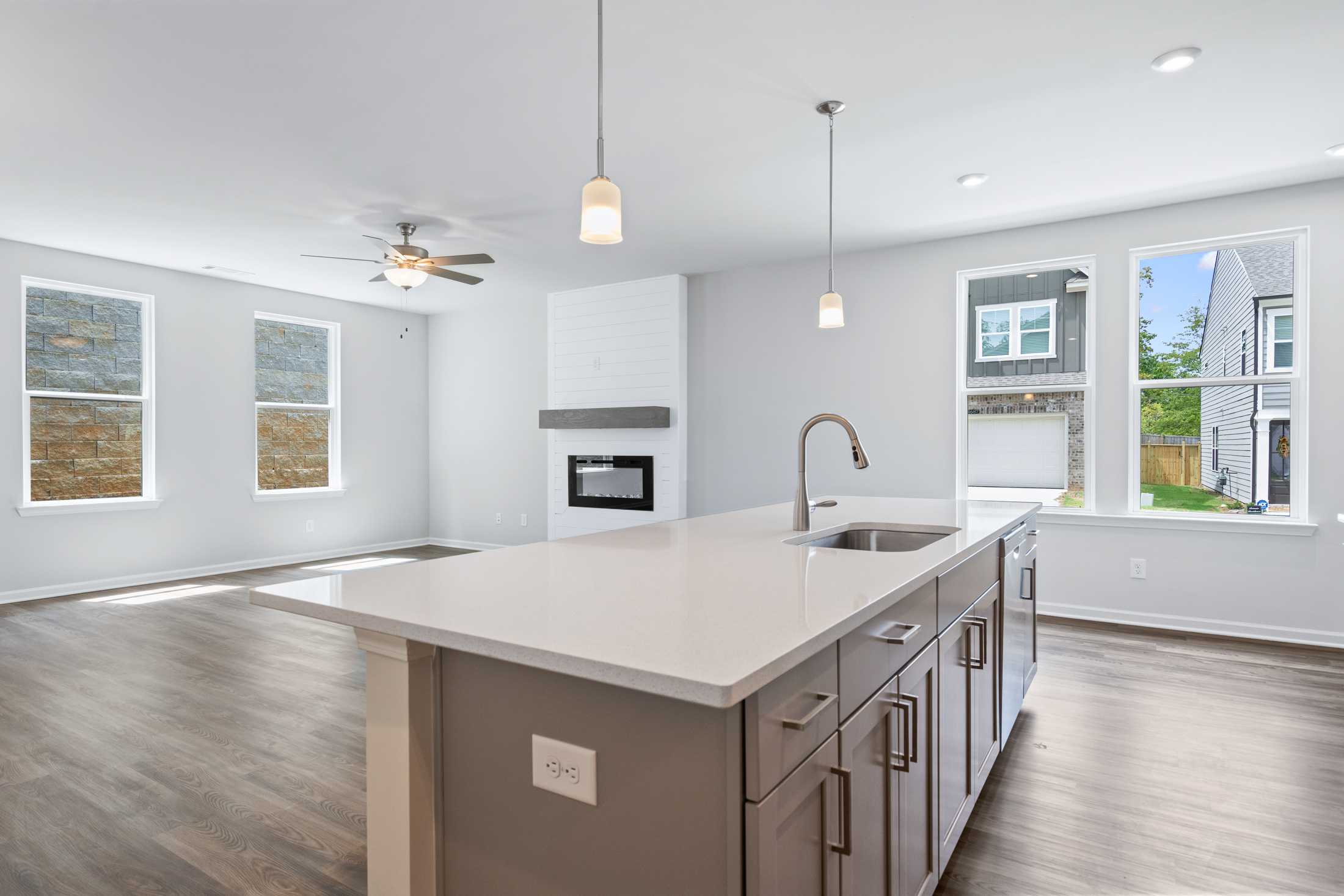 Open-concept kitchen in The Cary A with white quartz island, stainless sink, gray cabinets, pendant lights, and adjacent living space