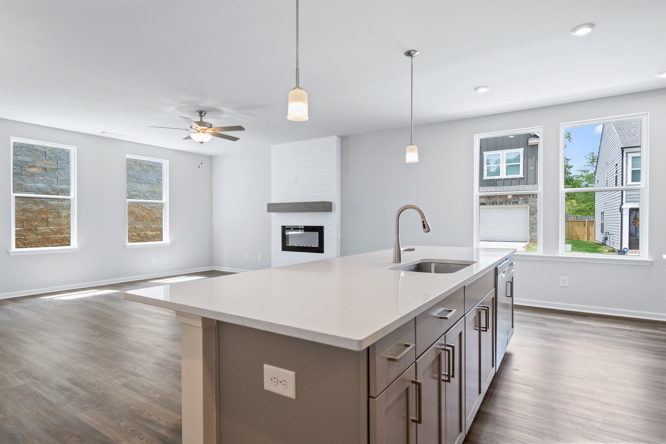 Open-concept kitchen in The Cary A with white quartz island, stainless sink, gray cabinets, pendant lights, and adjacent living space