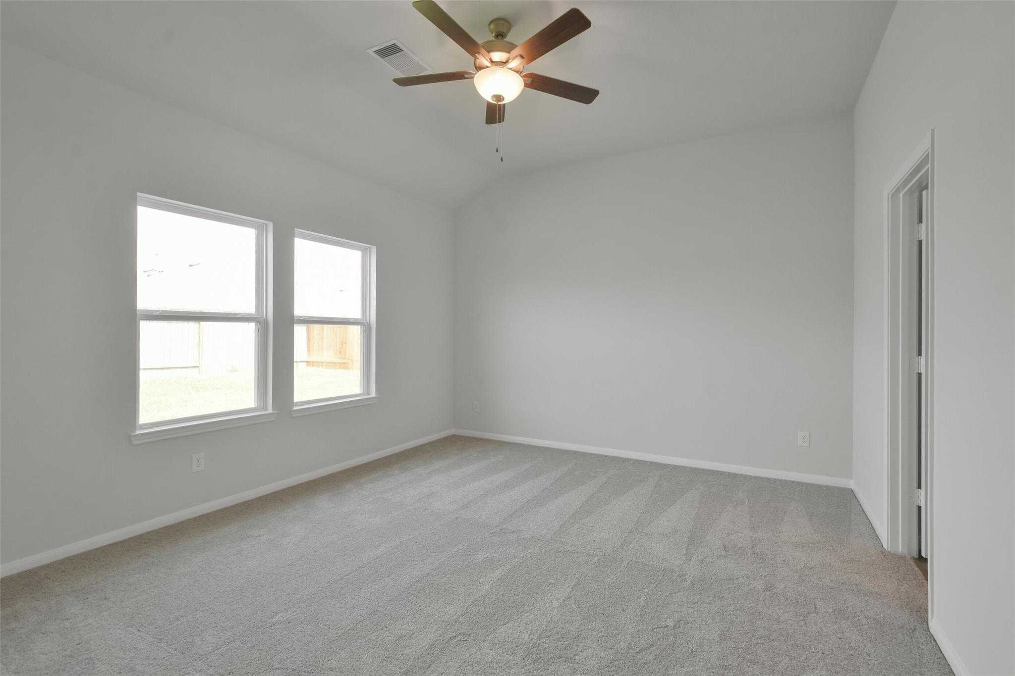 Bright bedroom with vaulted ceiling, gray carpet, ceiling fan, and large windows in Davidson Homes The Tierra A, Dayton, Texas