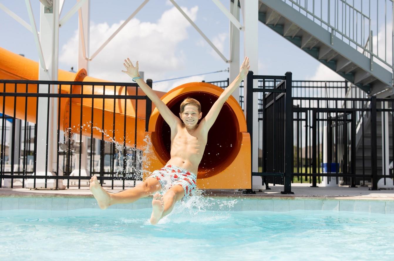 Man sliding down orange waterslide into blue community pool at Sunterra, Katy, Texas