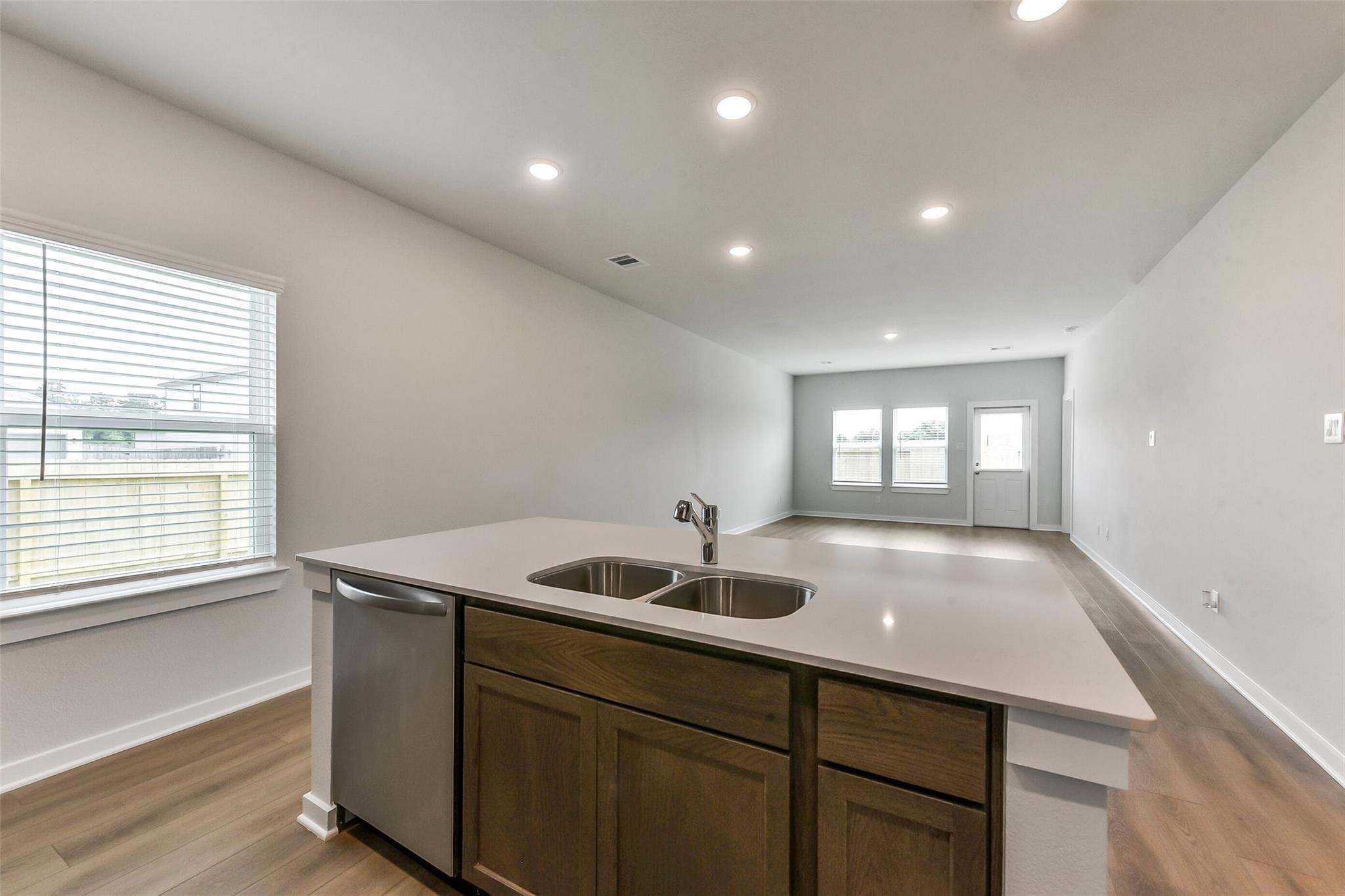 Open-concept kitchen with central island, quartz counters, double sink, stainless dishwasher, and wood cabinets in The Sabine F, Dayton TX