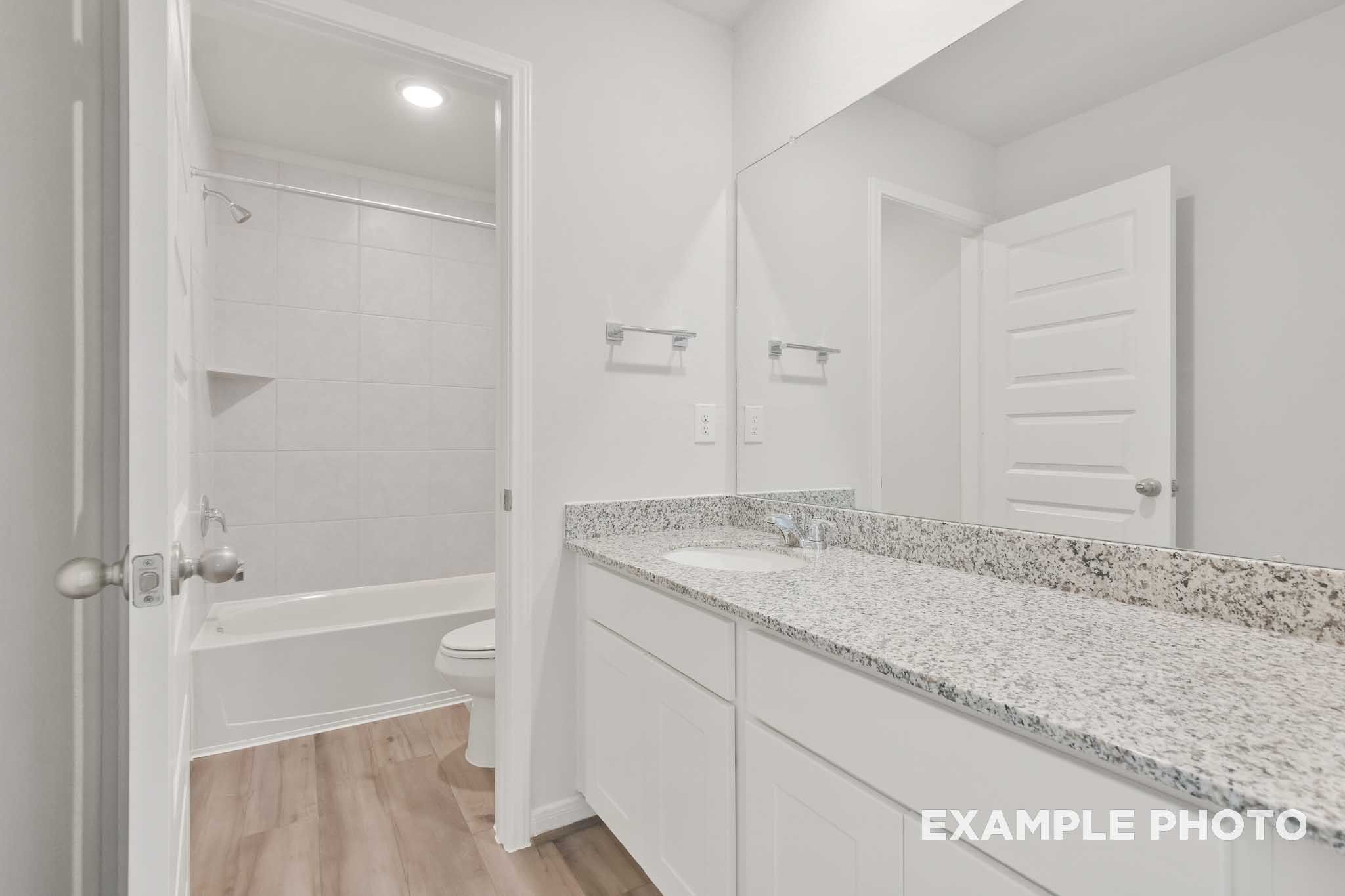 Bathroom in The Brazos by Davidson Homes featuring granite vanity, white cabinetry, and tile tub shower combo