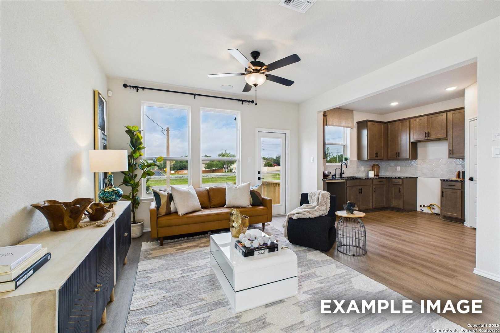 Open-concept living room with leather sofa, plants, and large windows adjoining modern kitchen in Davidson Homes The Florence C, San Antonio