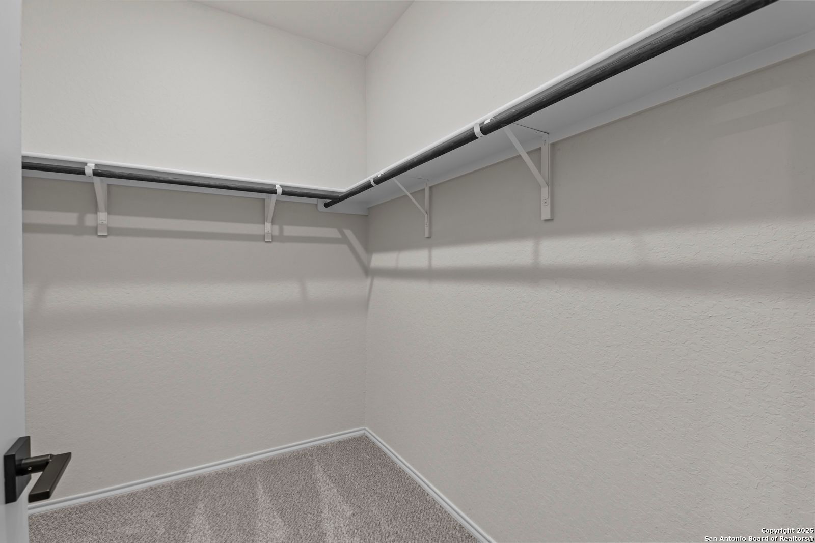 Spacious walk-in closet with double black hanging rods, neutral beige walls, and carpet floor in Davidson Homes The Douglas C, Seguin, Texas