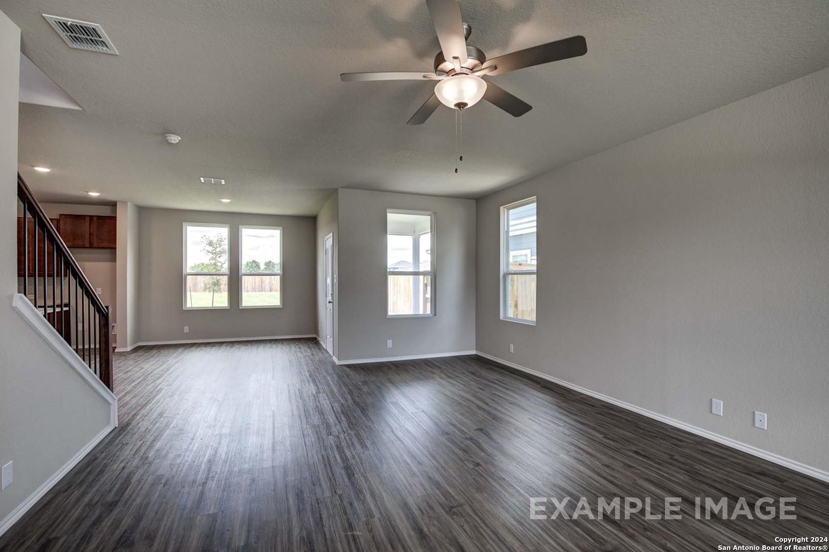 Spacious open living room with hardwood floors, ceiling fan, large windows, and staircase in Davidson Homes The Murray J, Bricewood, San Antonio