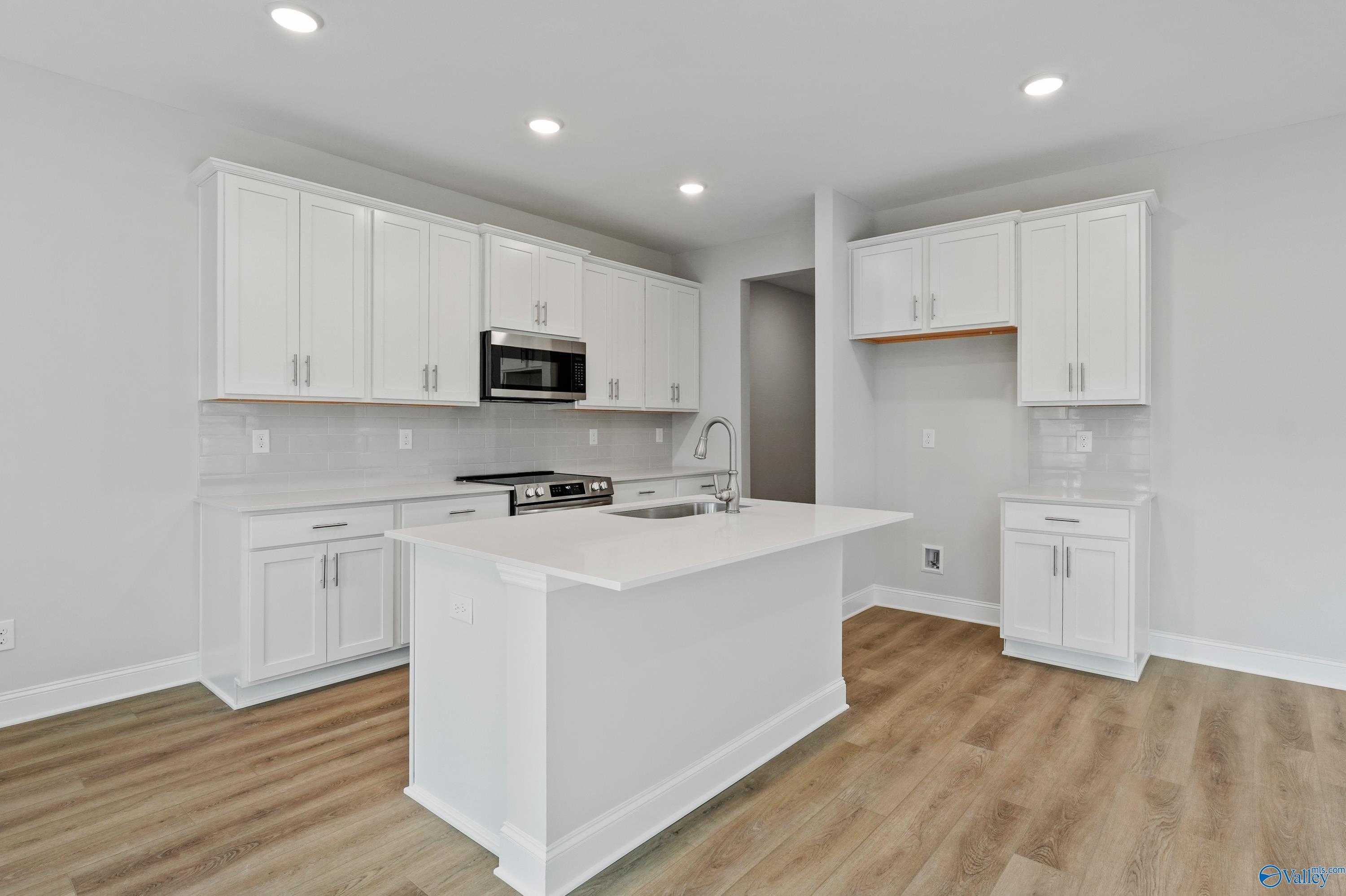 Modern white kitchen island with stainless steel appliances and quartz counters in Davidson Homes The Camden, Huntsville AL