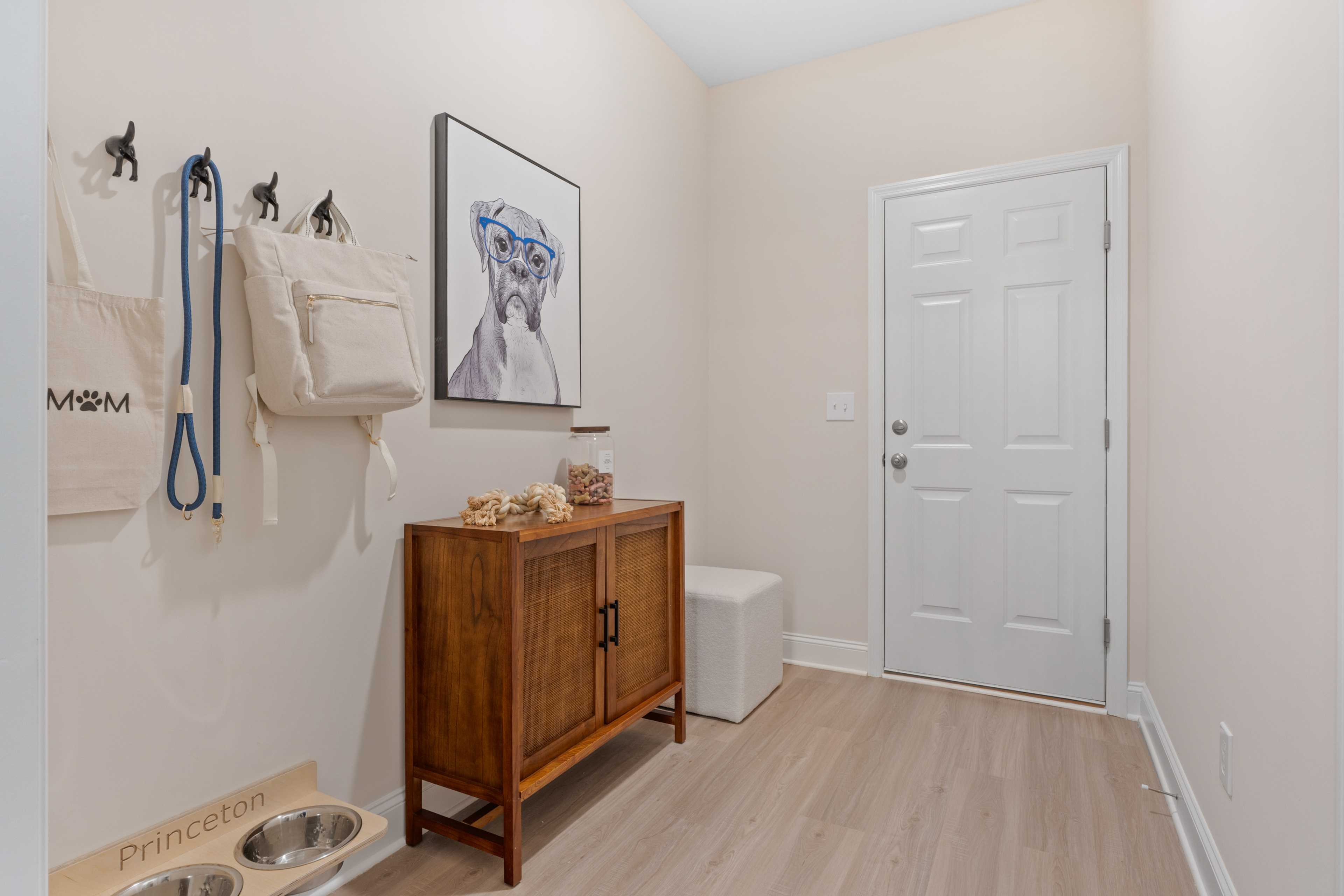 Cozy mudroom at Pavilion in Huntsville AL with pet station, wooden cabinet, dog portrait art, beige walls, and hooks for leashes