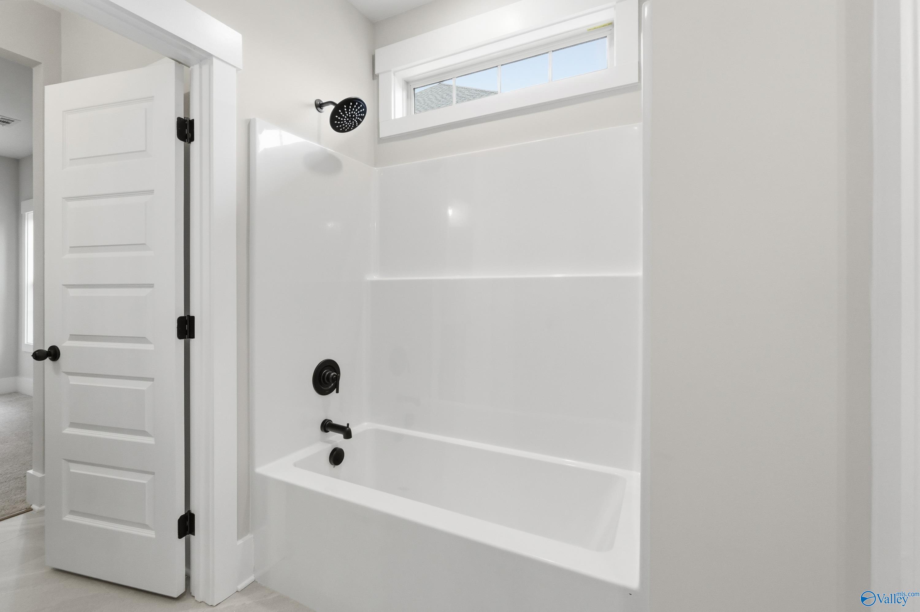 Modern bathroom with white tiled glass shower enclosure, deep soaking tub, and neutral walls in The Finleigh home, Meridianville, Alabama