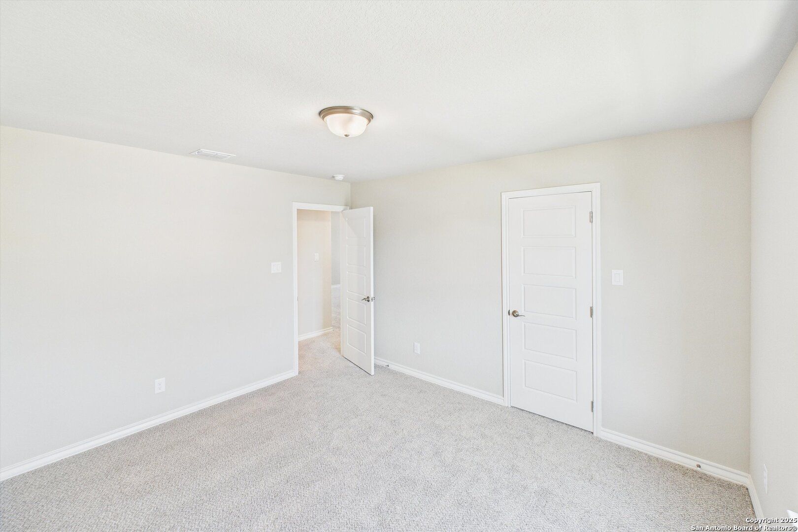 Bright empty secondary bedroom with beige walls, gray carpet, and white doors in Davidson Homes The Jennings H, Ladera, San Antonio