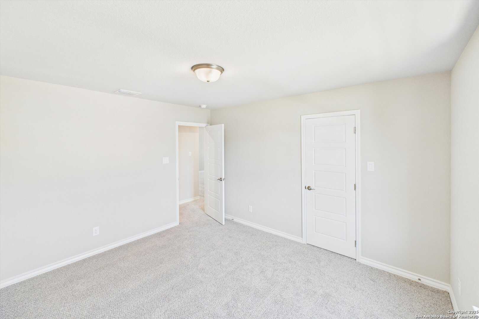 Bright empty secondary bedroom with beige walls, gray carpet, and white doors in Davidson Homes The Jennings H, Ladera, San Antonio