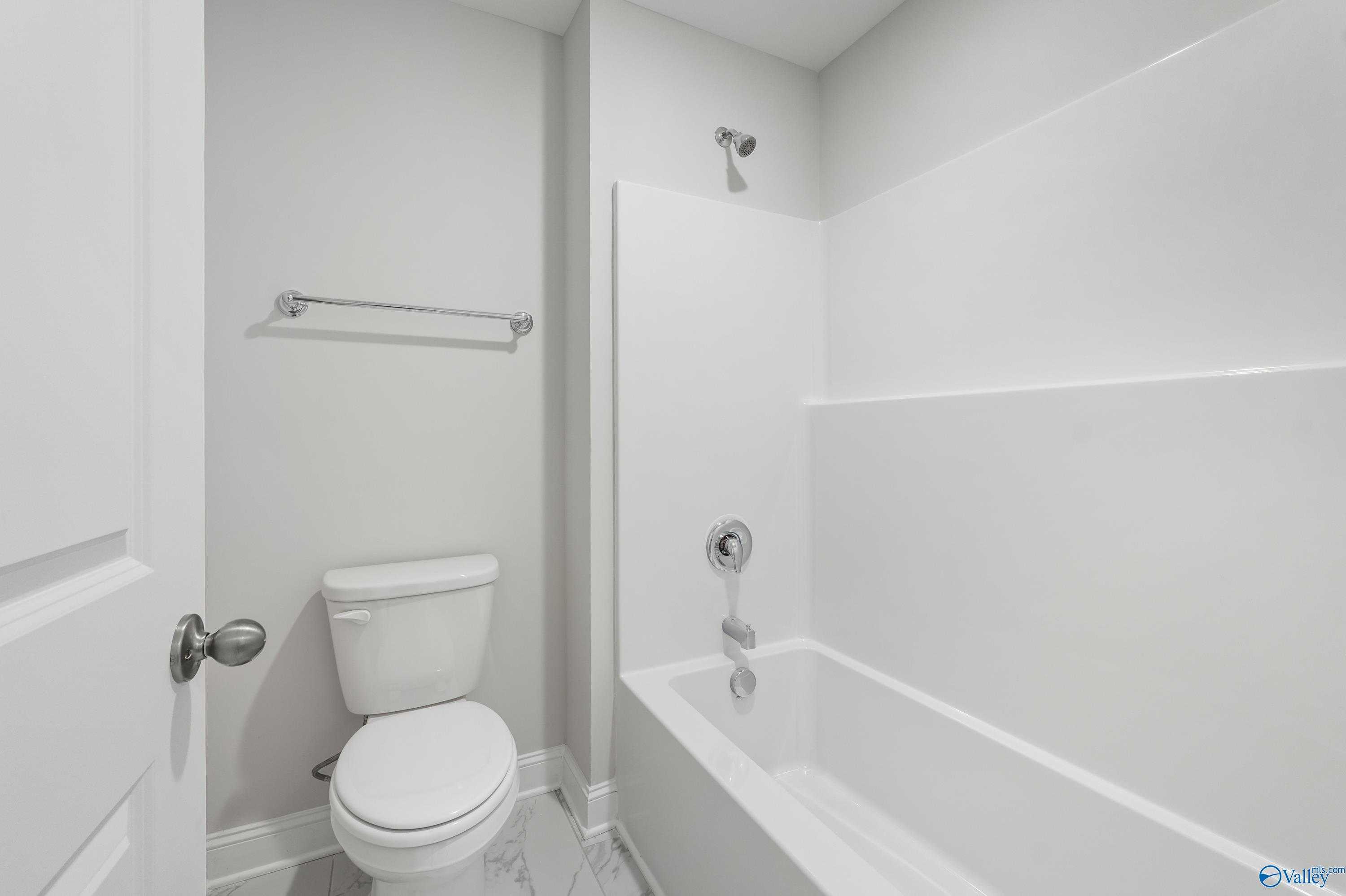 Bright white tub-shower combo, toilet, and towel bar in modern bathroom of The Camden B by Davidson Homes, Huntsville, AL