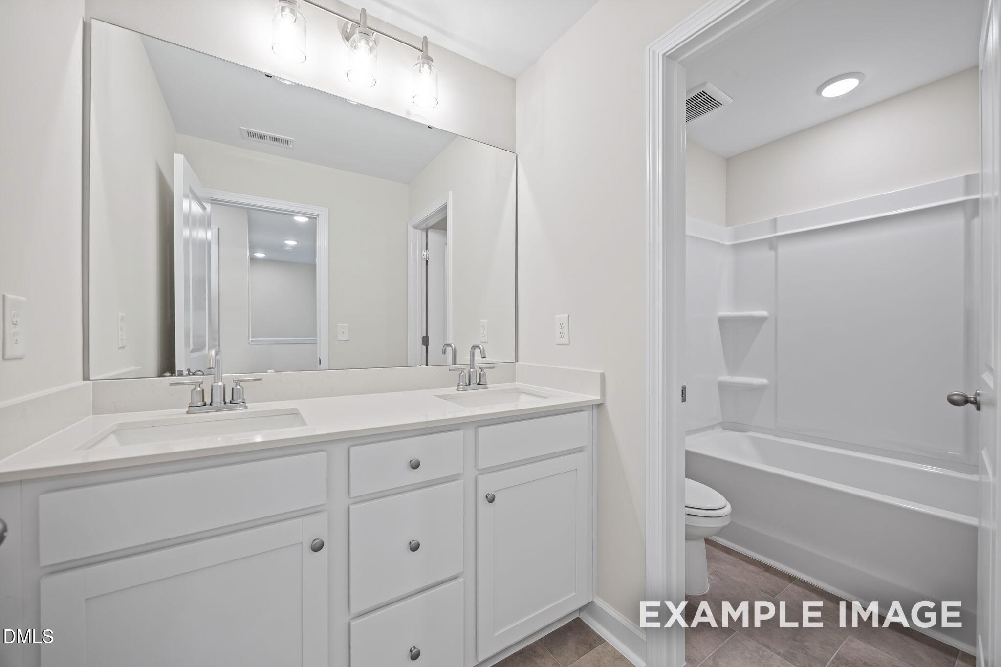Modern double vanity bathroom with white shaker cabinets, quartz counters, and large mirror in Davidson Homes The Avery, Knightdale, NC
