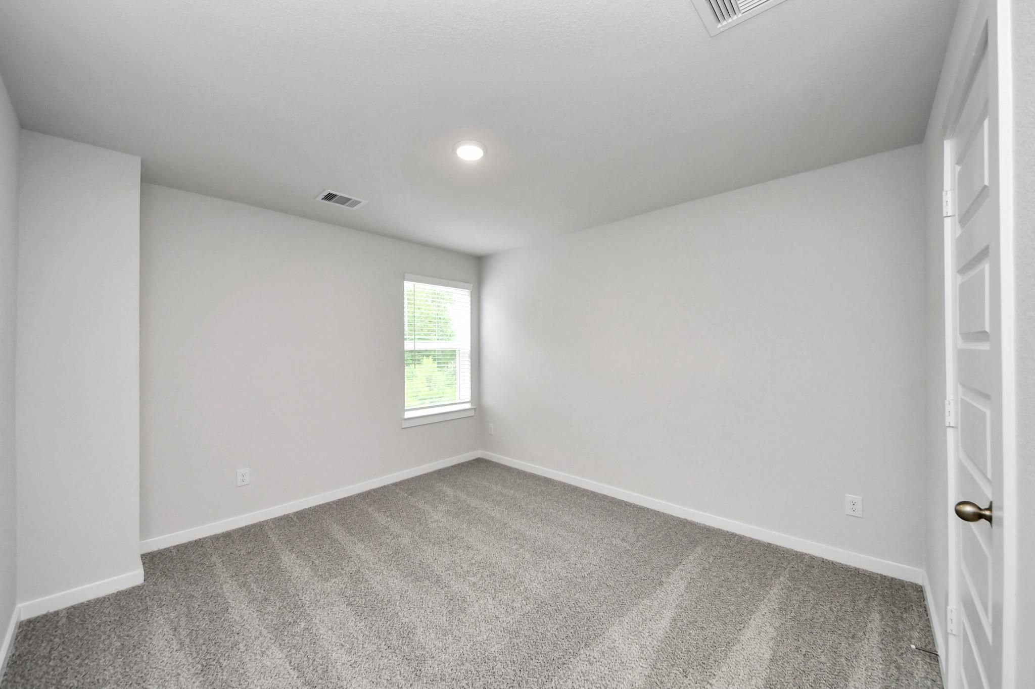 Spacious secondary bedroom with neutral carpet in The Sabine E floor plan at Liberty Estates in Cleveland, Texas.