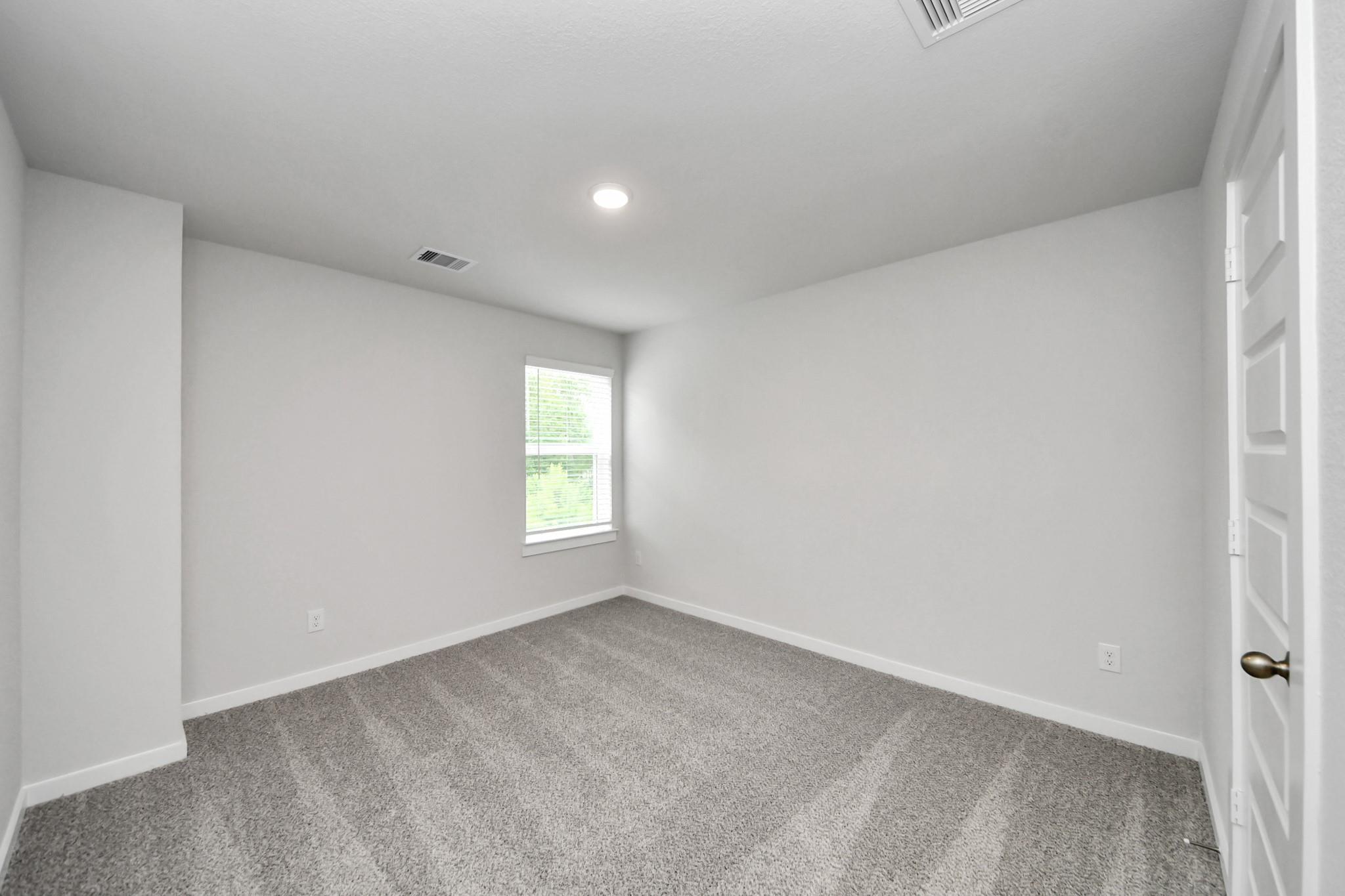 Spacious secondary bedroom with neutral carpet in The Sabine E floor plan at Liberty Estates in Cleveland, Texas.