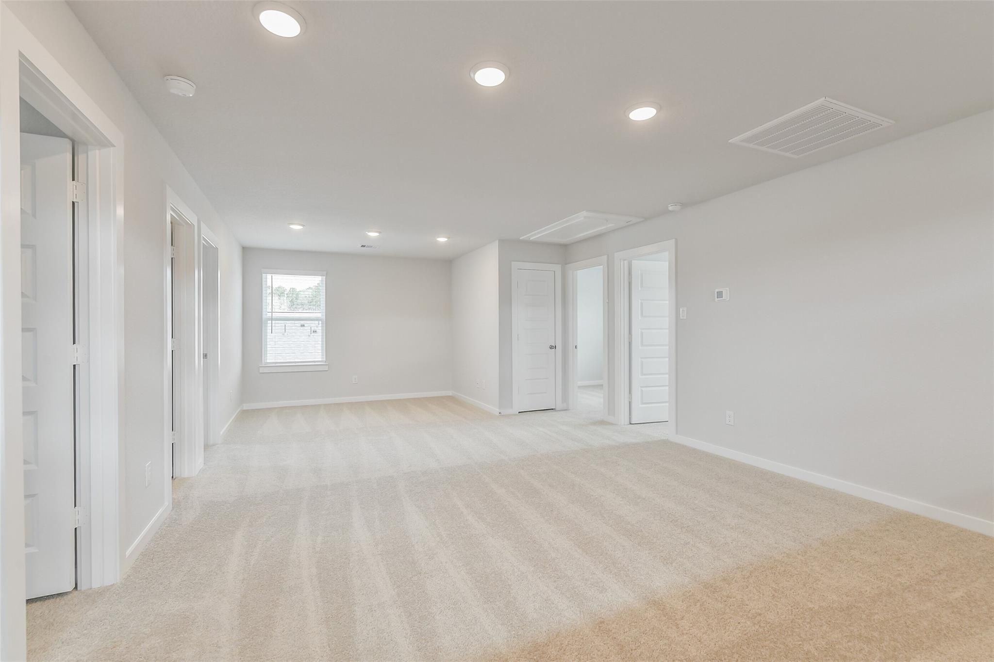 Bright upstairs hallway with multiple bedroom doors, beige carpet, and recessed lights in The Brazos E home, Cleveland, Texas