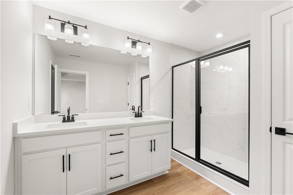 Modern master bathroom with double white vanity, large mirrors, and glass shower enclosure in Davidson Homes The Cary A, Winder, GA