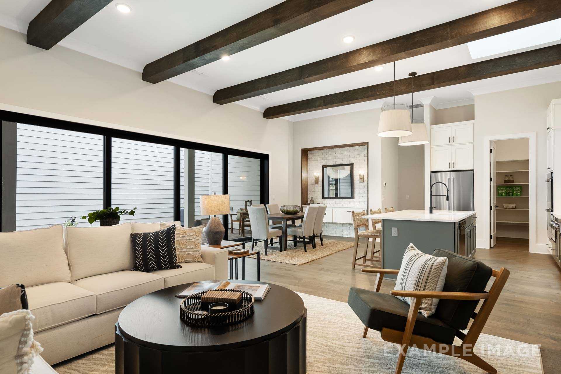 Spacious open-concept living room at Manor Estates in Marietta GA with exposed wood beams, beige sofa, dining table, and kitchen island
