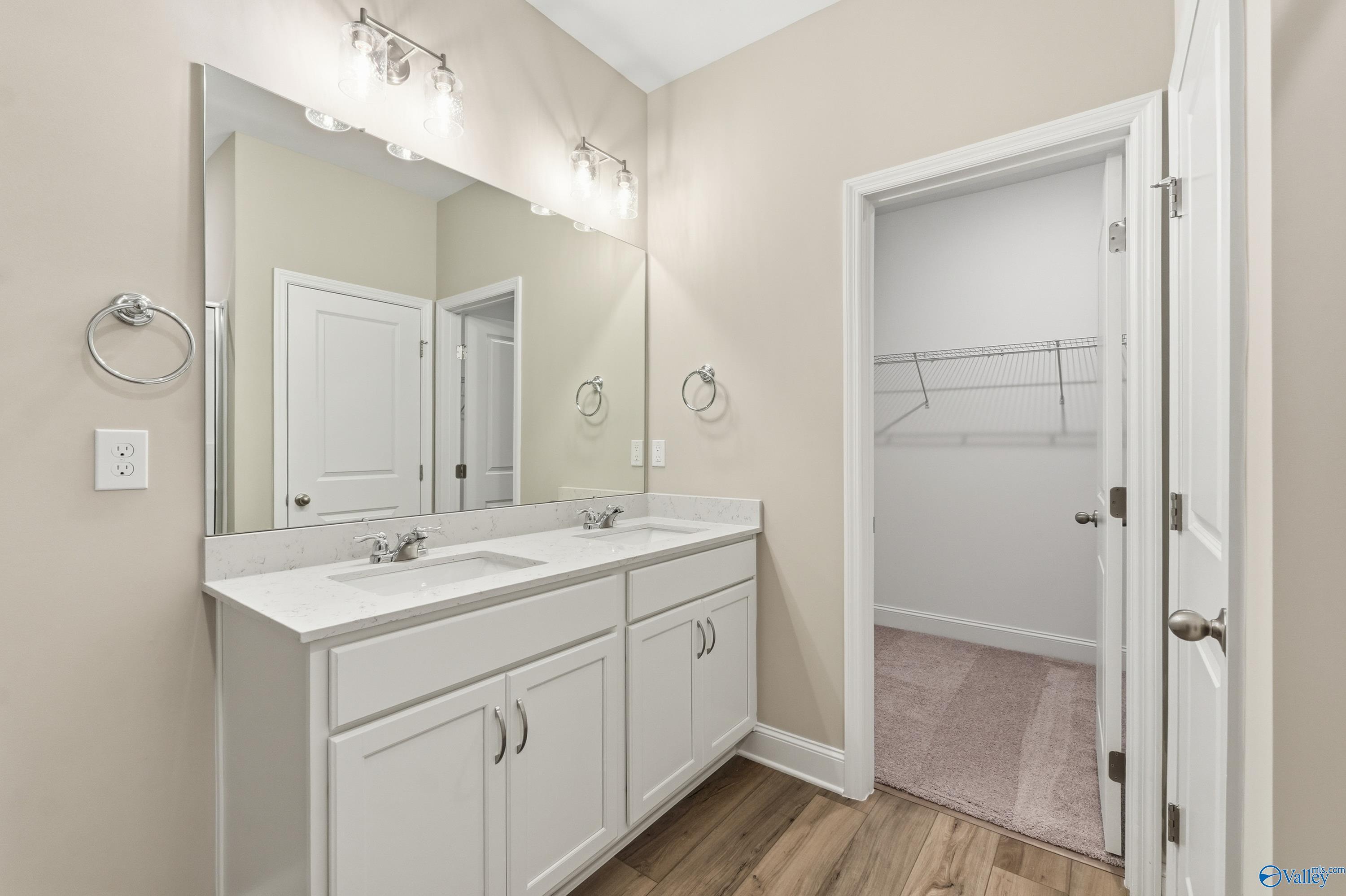Modern master bathroom featuring double vanity sinks, white cabinets, mirrors, and adjacent closet in Davidson Homes The Franklin C, New Market, AL