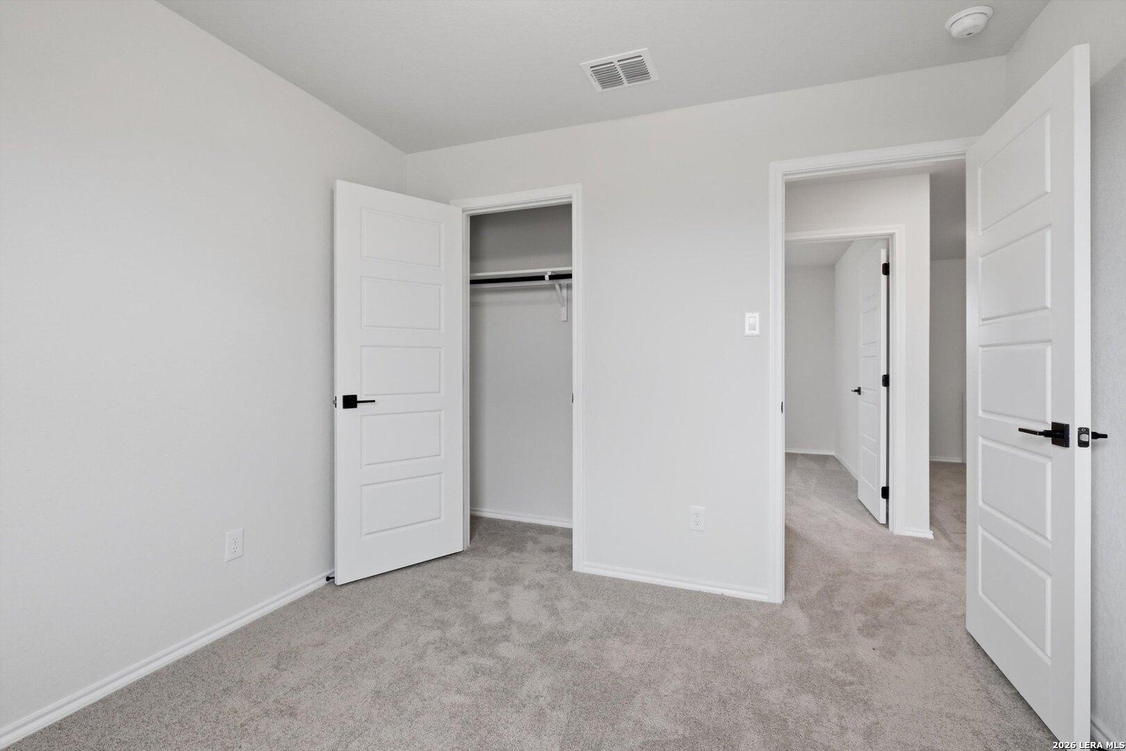 Bright secondary bedroom with open closet doors and adjacent bath entry on plush gray carpet in Davidson Homes The Blanco C, Agave San Antonio