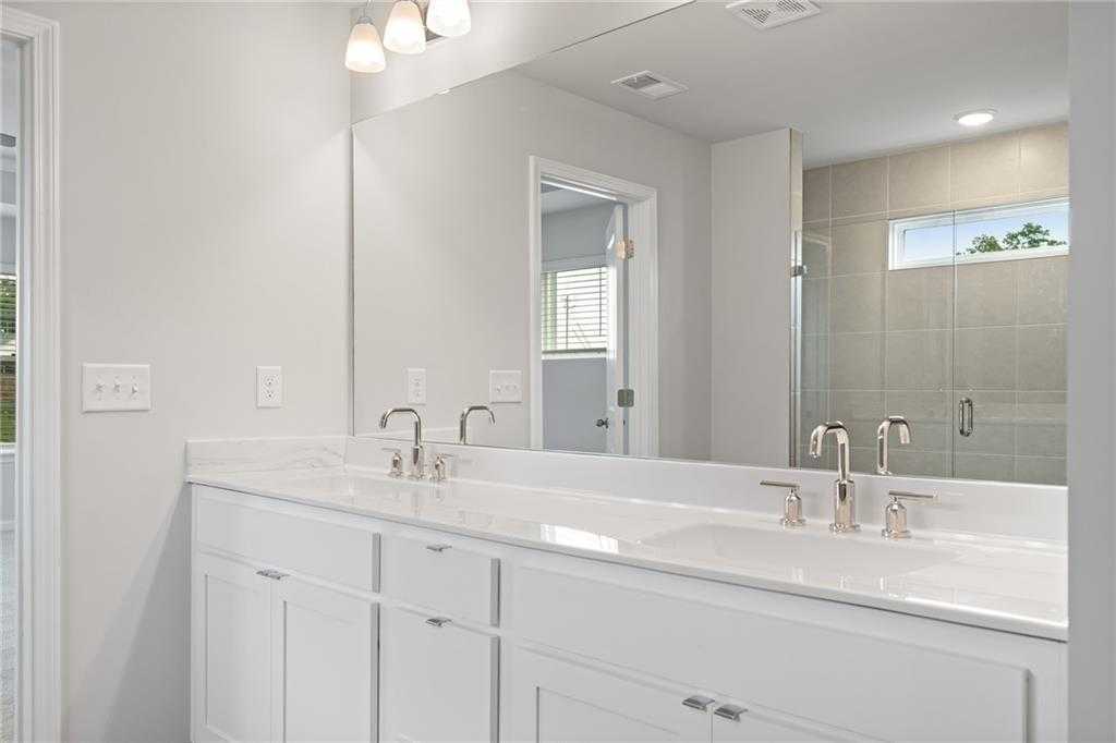 Modern master bathroom featuring double white vanity, chrome faucets, large mirror, and glass shower in Davidson Homes The Hickory B, Winder, Georgia
