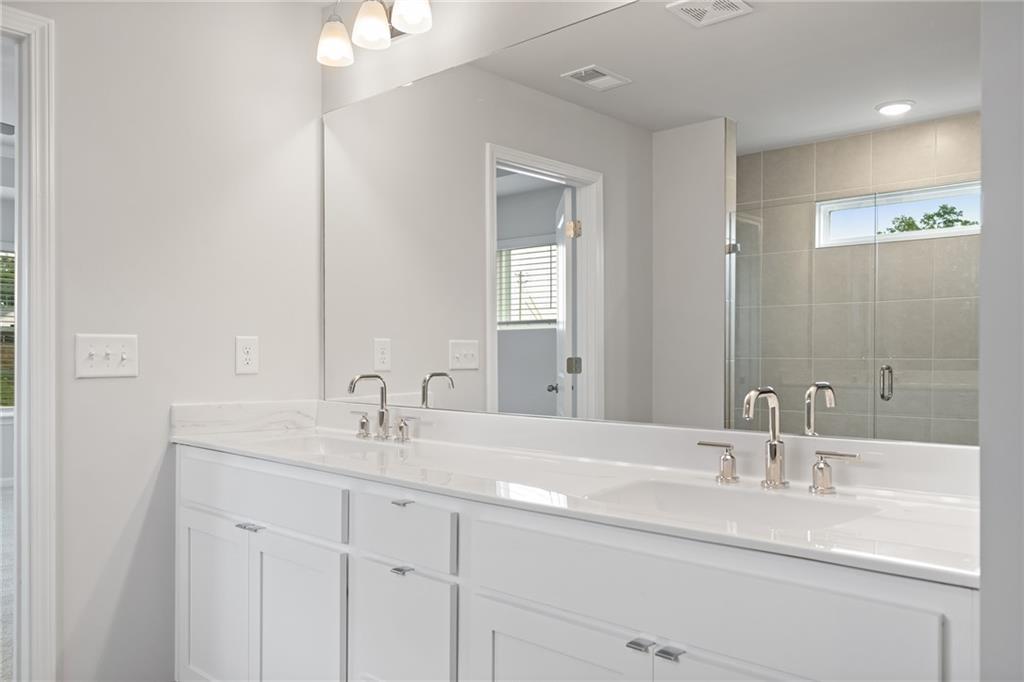 Elegant master bath double vanity with white cabinets, chrome faucets, and large mirror in Davidson Homes The Hickory A, Winder GA