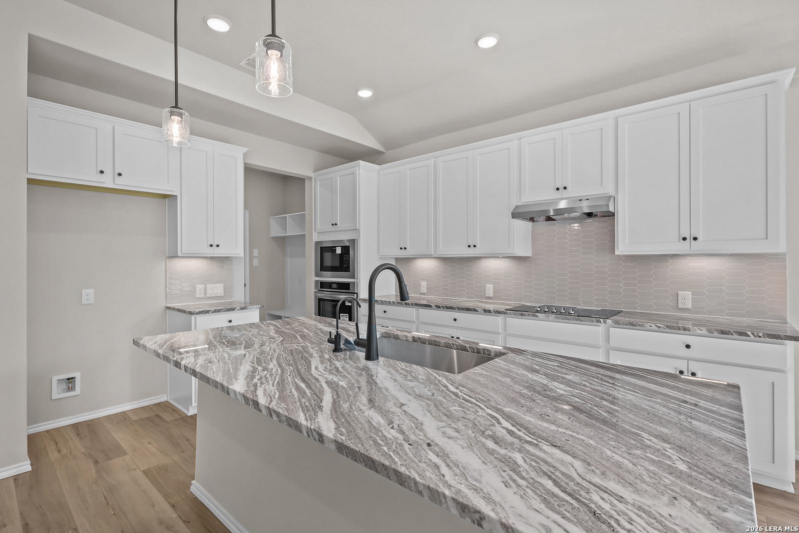 Modern kitchen with granite island, white shaker cabinets, and pendant lights in Davidson Homes The Sequoia C, Royal Crest, San Antonio