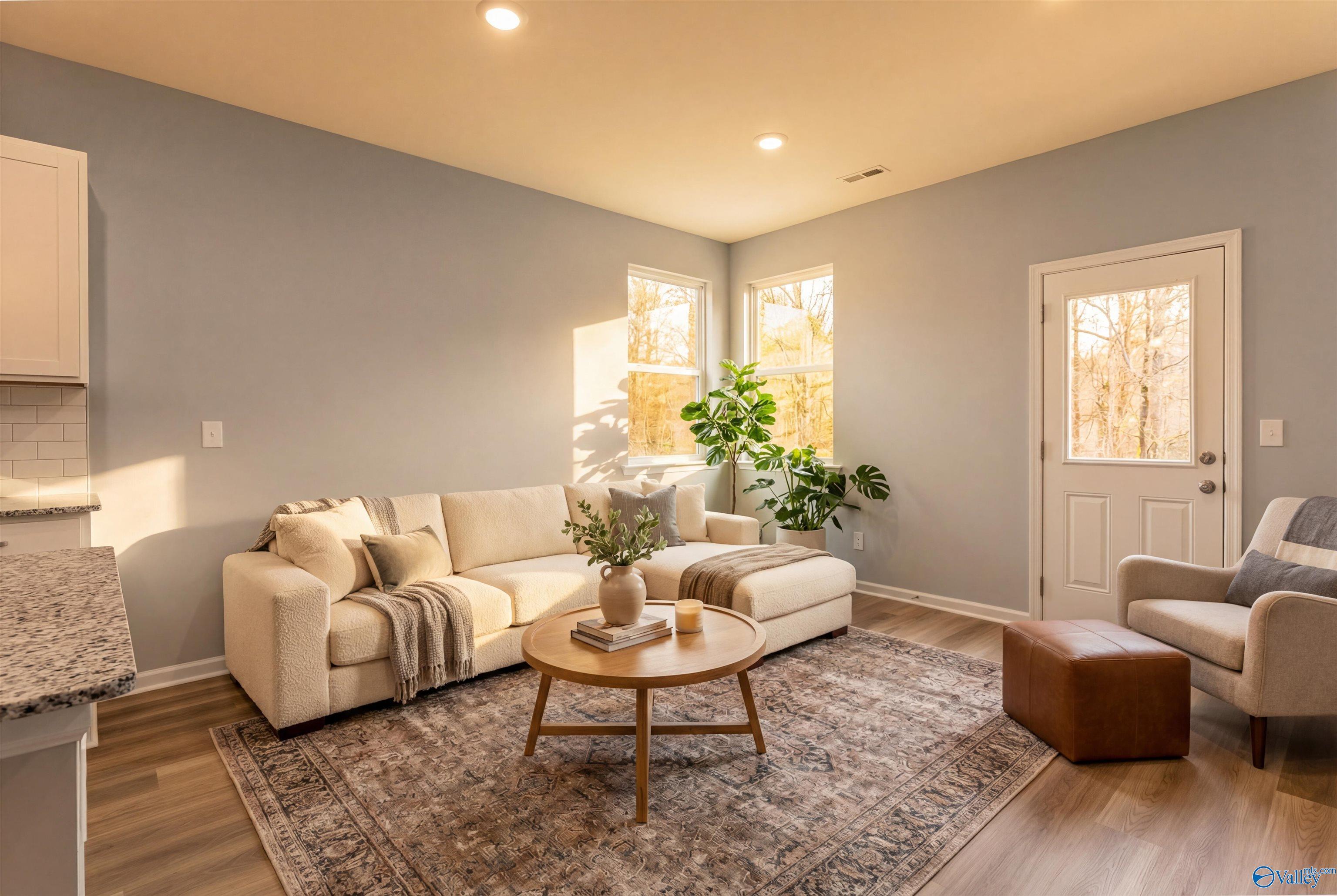 Cozy living room with beige sofa, armchair, potted plants, and sunlit windows in The Phoenix 3-bedroom home, Hazel Green, Alabama