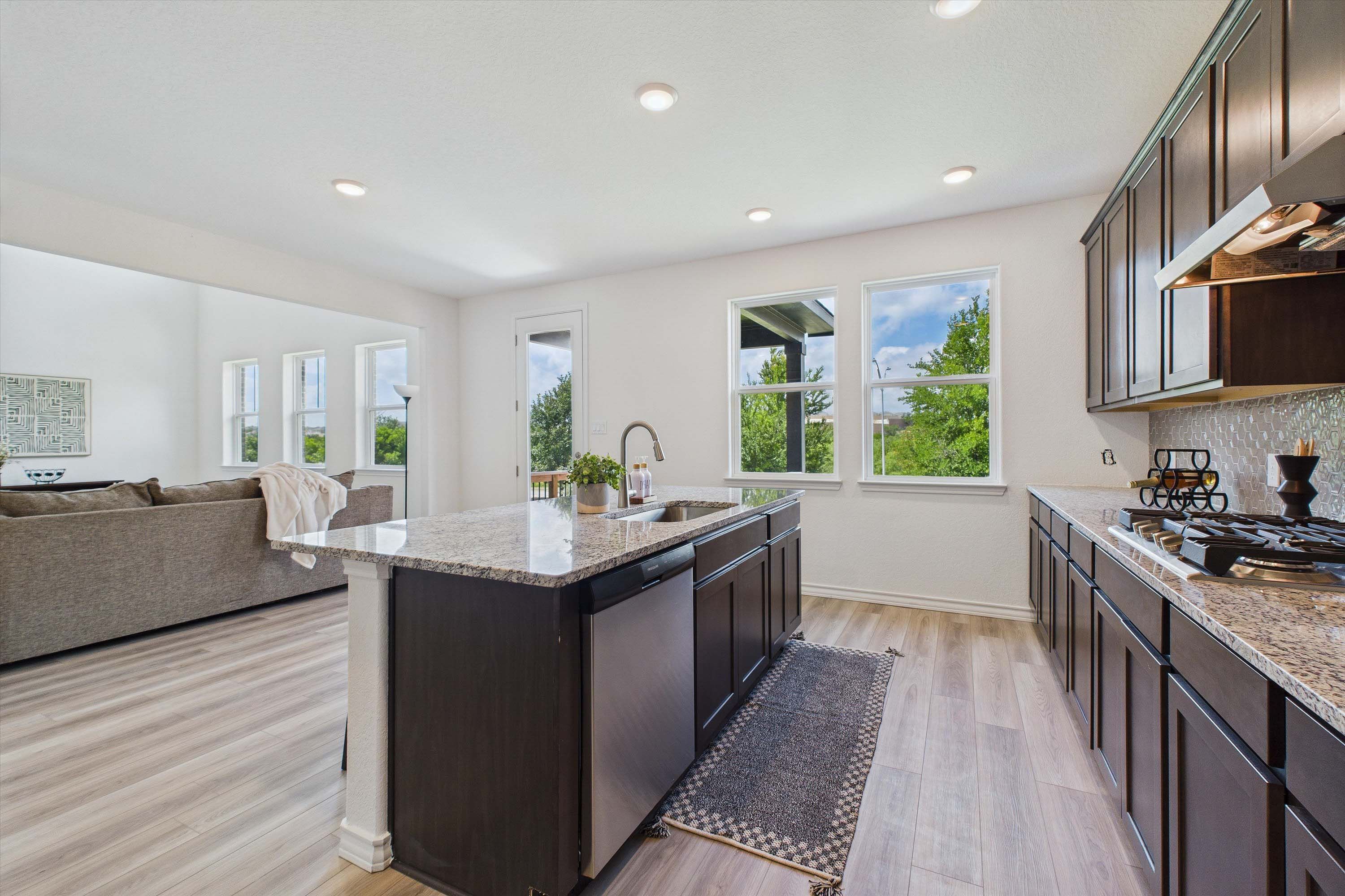 Open-concept kitchen in The Danbury featuring dark cabinetry, granite countertops, and an island overlooking the living room.