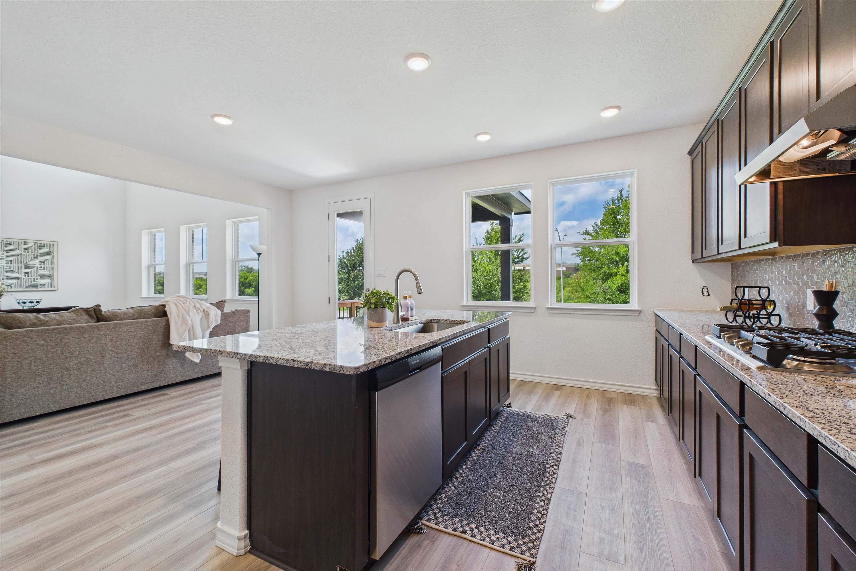 Open-concept kitchen in The Danbury featuring dark cabinetry, granite countertops, and an island overlooking the living room.