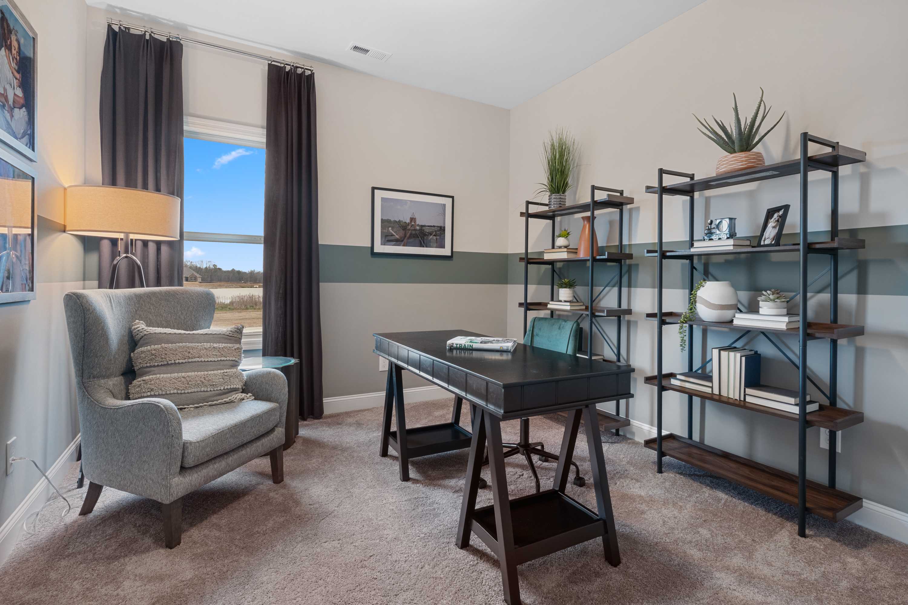 Cozy home office at The Retreat at Cain Park in Hartselle AL with wooden desk, gray armchair, metal bookshelves, plants, and window view