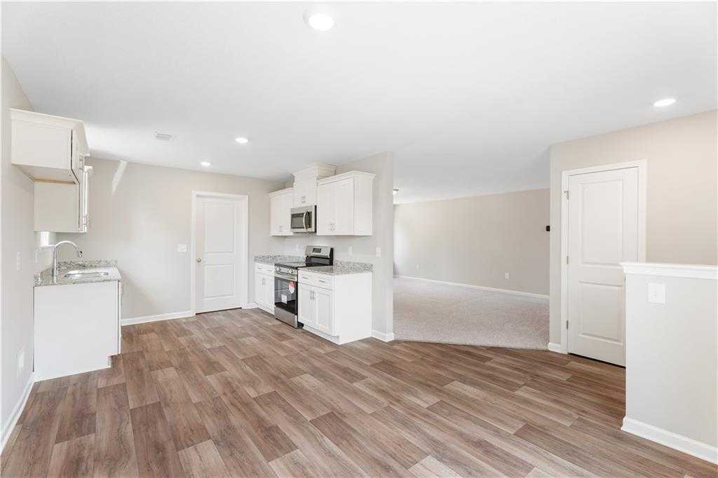 Modern open-concept kitchen with white cabinets, stainless appliances, and wood flooring in Evermore Homes The Washington, Phenix City, AL