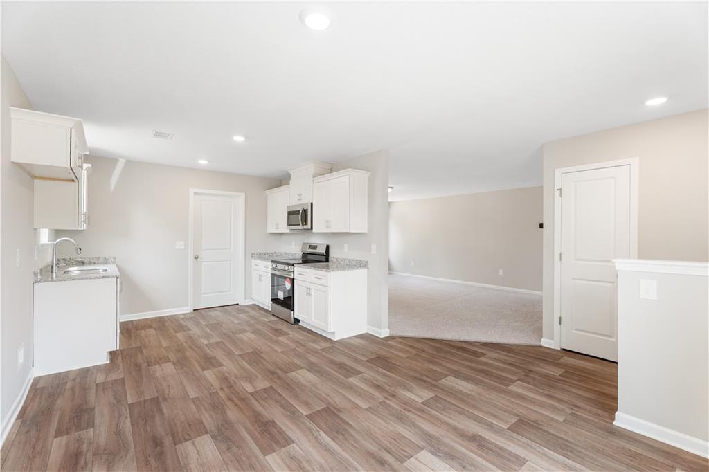 Modern open-concept kitchen with white cabinets, stainless appliances, and wood flooring in Evermore Homes The Washington, Phenix City, AL