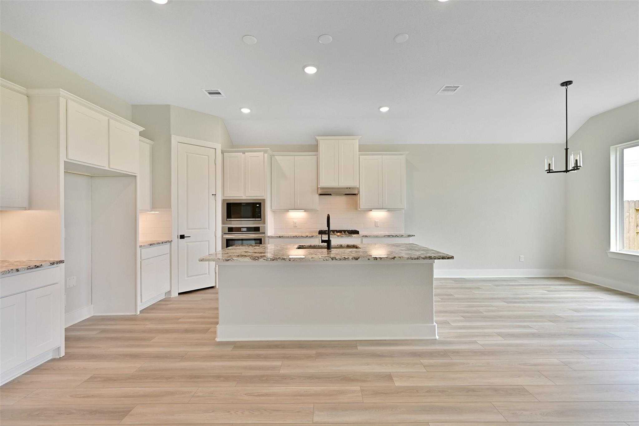 Modern white kitchen with large island, quartz counters, stainless appliances in Davidson Homes The Edward C, Lago Mar, Texas City