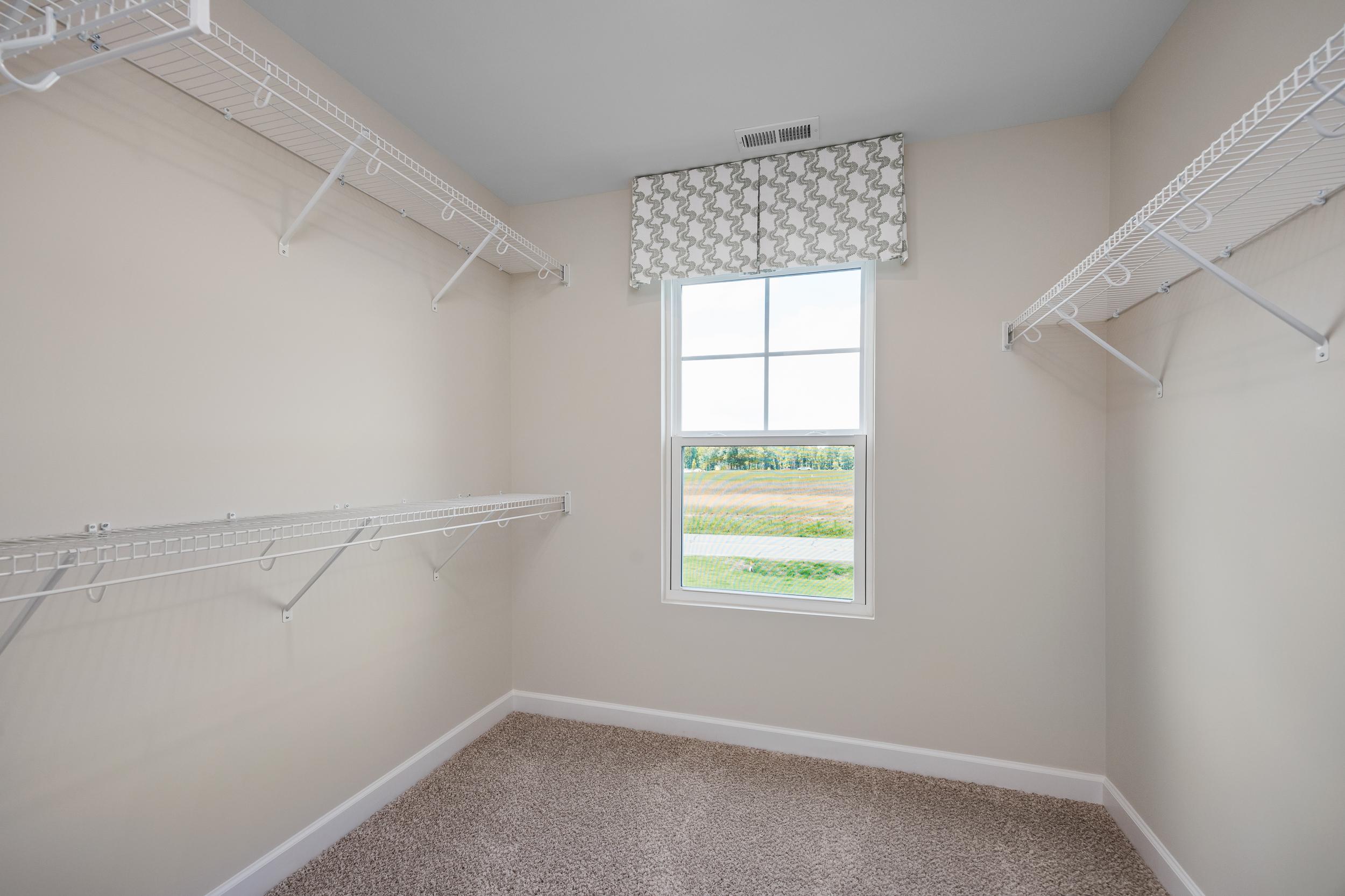 Spacious walk-in closet with white wire shelving, valance window overlooking fields, and carpeted floor at Retreat at North Main in Lillington NC