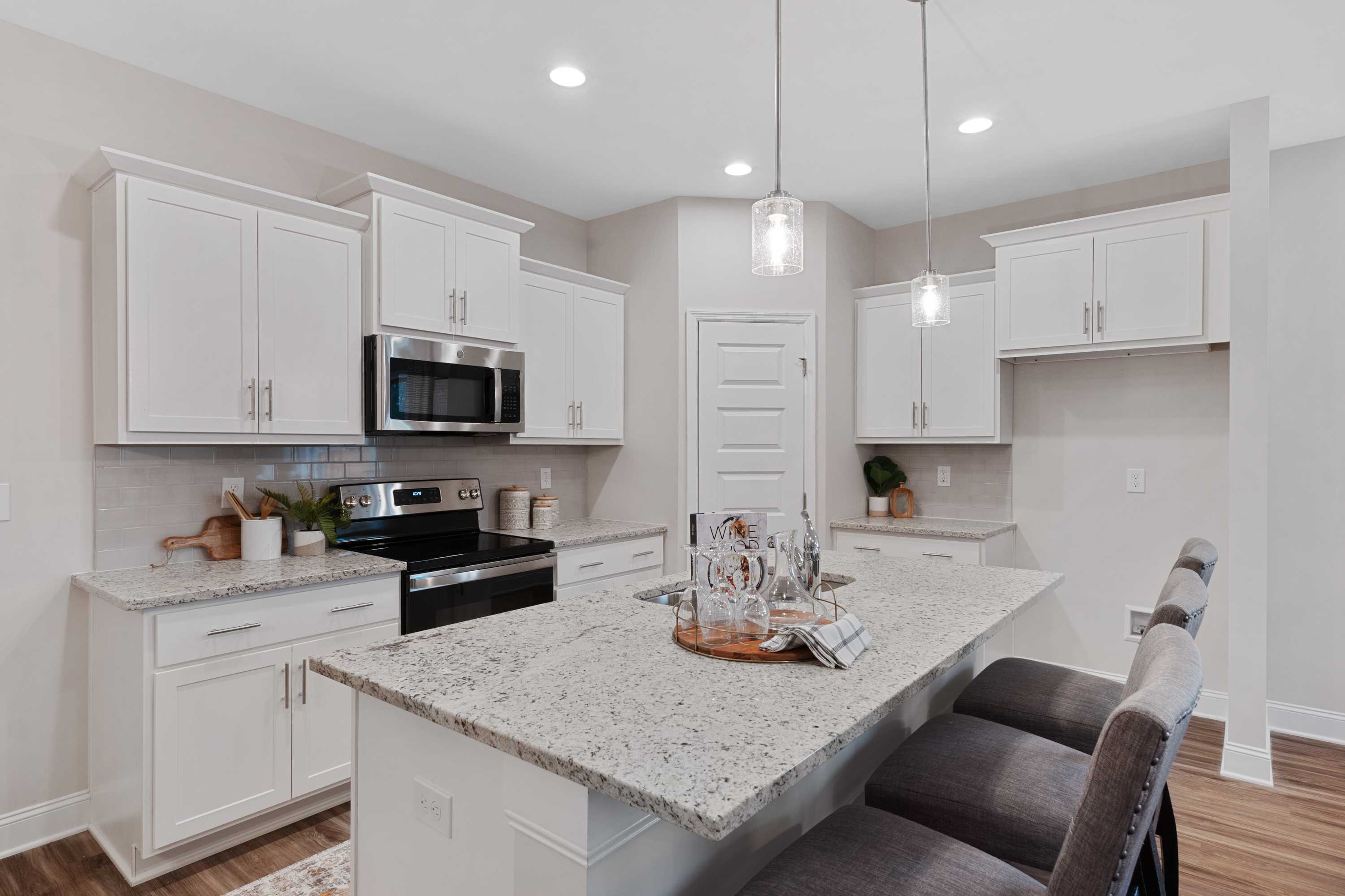 Modern white kitchen with stainless appliances, granite island, bar stools, and pendant lights at The Retreat at Cain Park, Hartselle AL