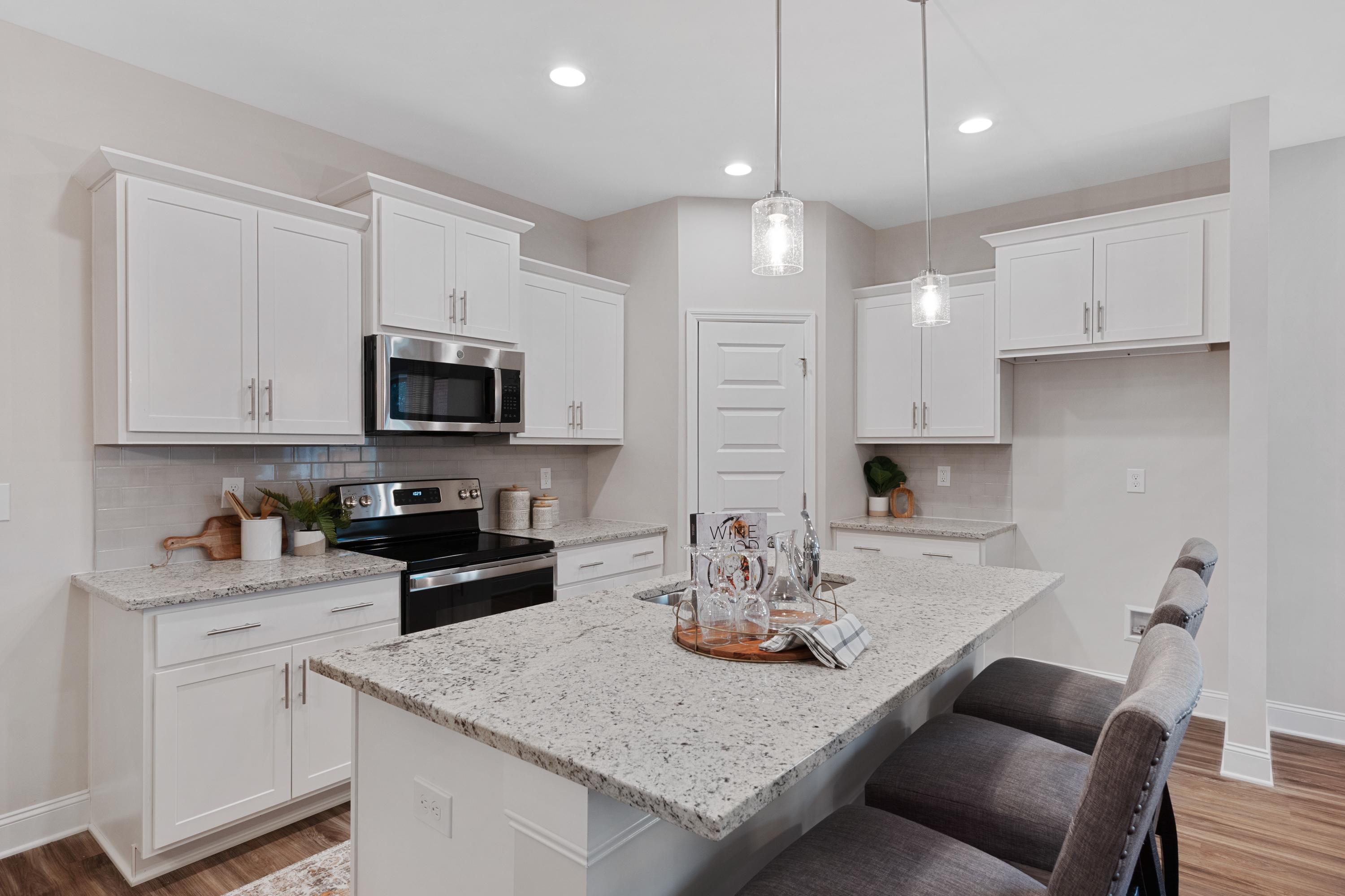 Modern white kitchen with stainless appliances, granite island, bar stools, and pendant lights at The Retreat at Cain Park, Hartselle AL