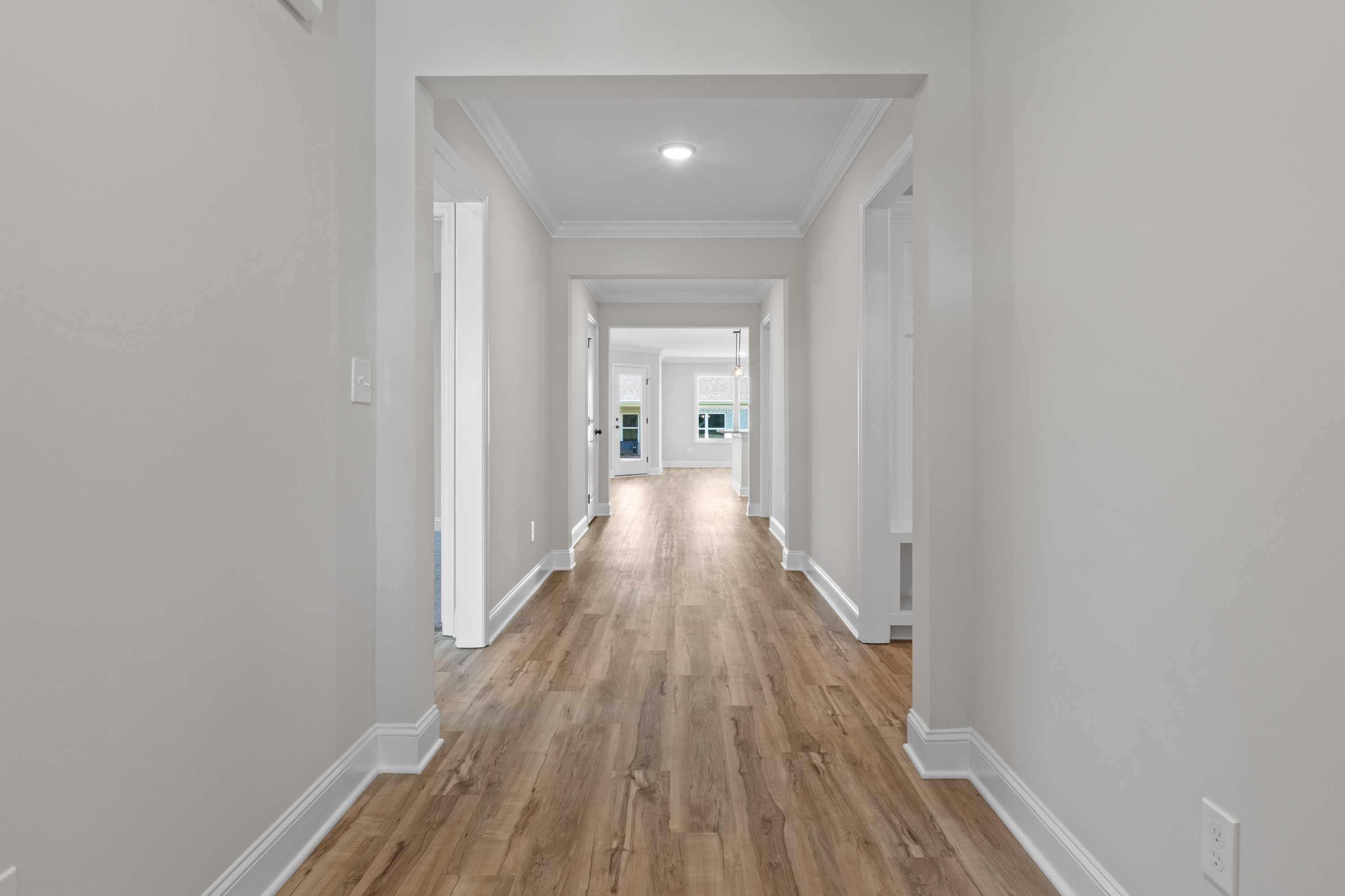 Spacious hallway in The Everett C home featuring light oak hardwood floors, white walls, and arched doorways