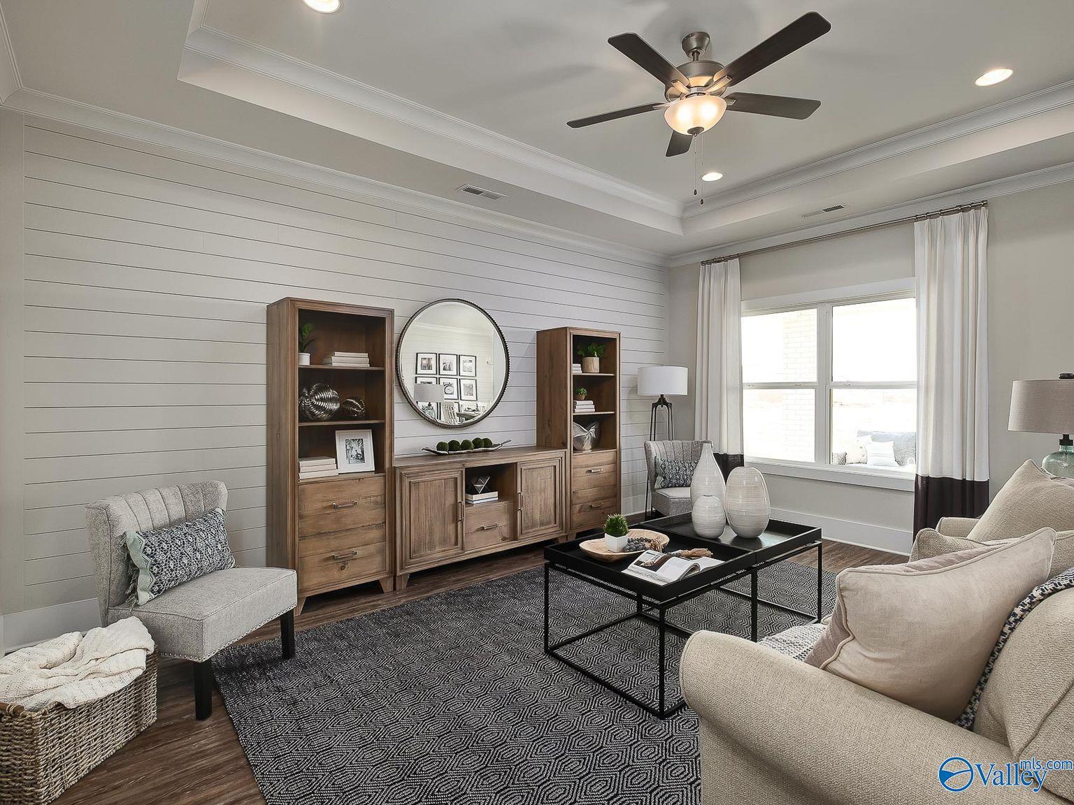 Cozy living room with shiplap walls, beige sofa, wooden built-ins, round mirror, and large windows in Davidson Homes The Everett, Toney Alabama