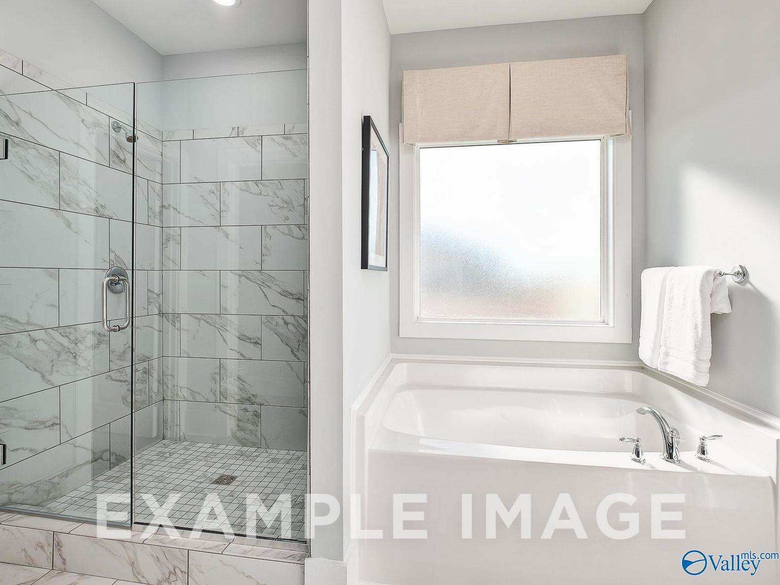 Modern master bathroom with frameless glass shower, white marble tiles, soaking tub, and frosted window in Davidson Homes The Everett B, Toney, AL