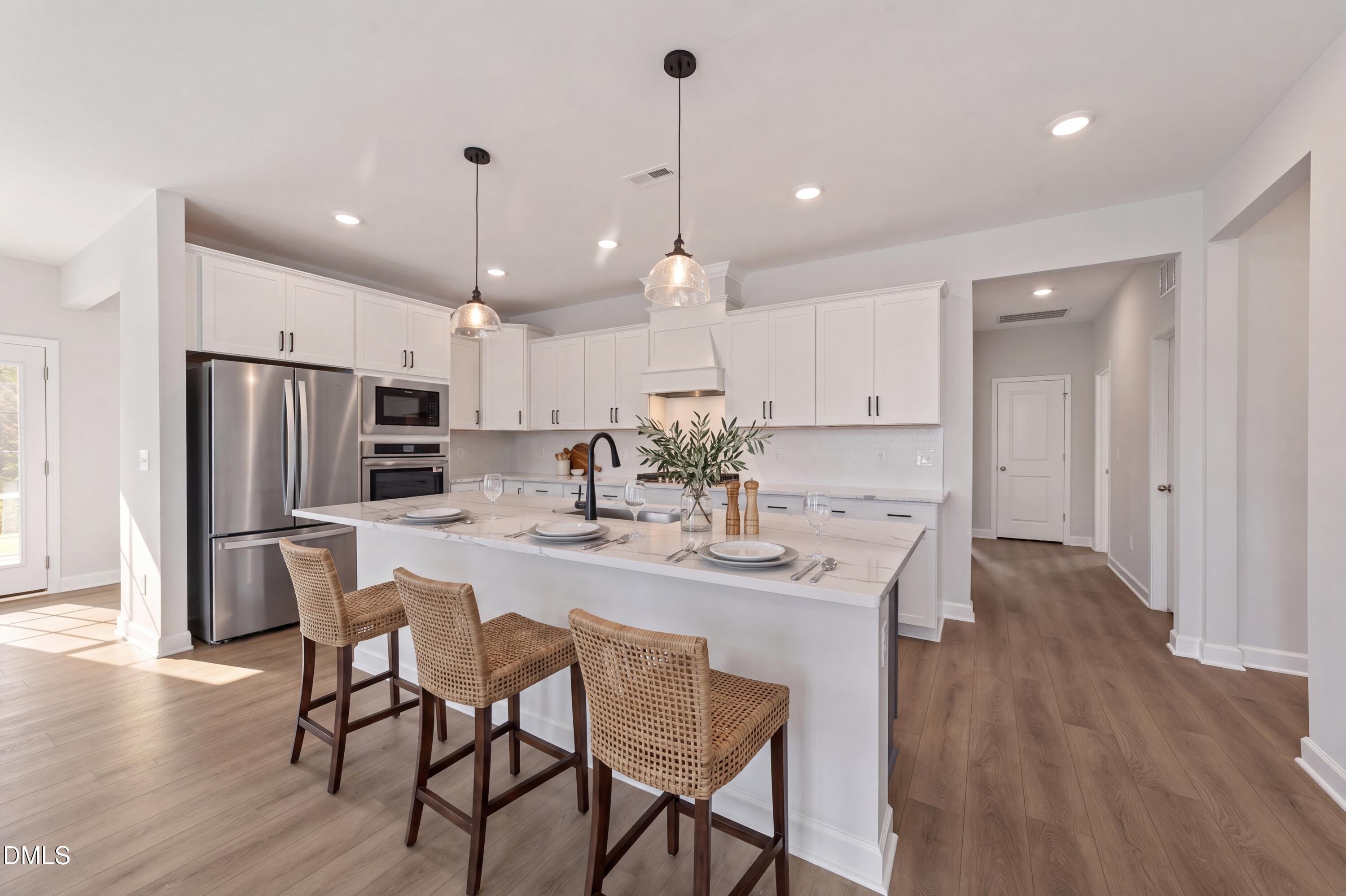 Modern kitchen with white cabinets, marble island, and wicker bar stools in The Magnolia B home at Wendell Ridge, NC.