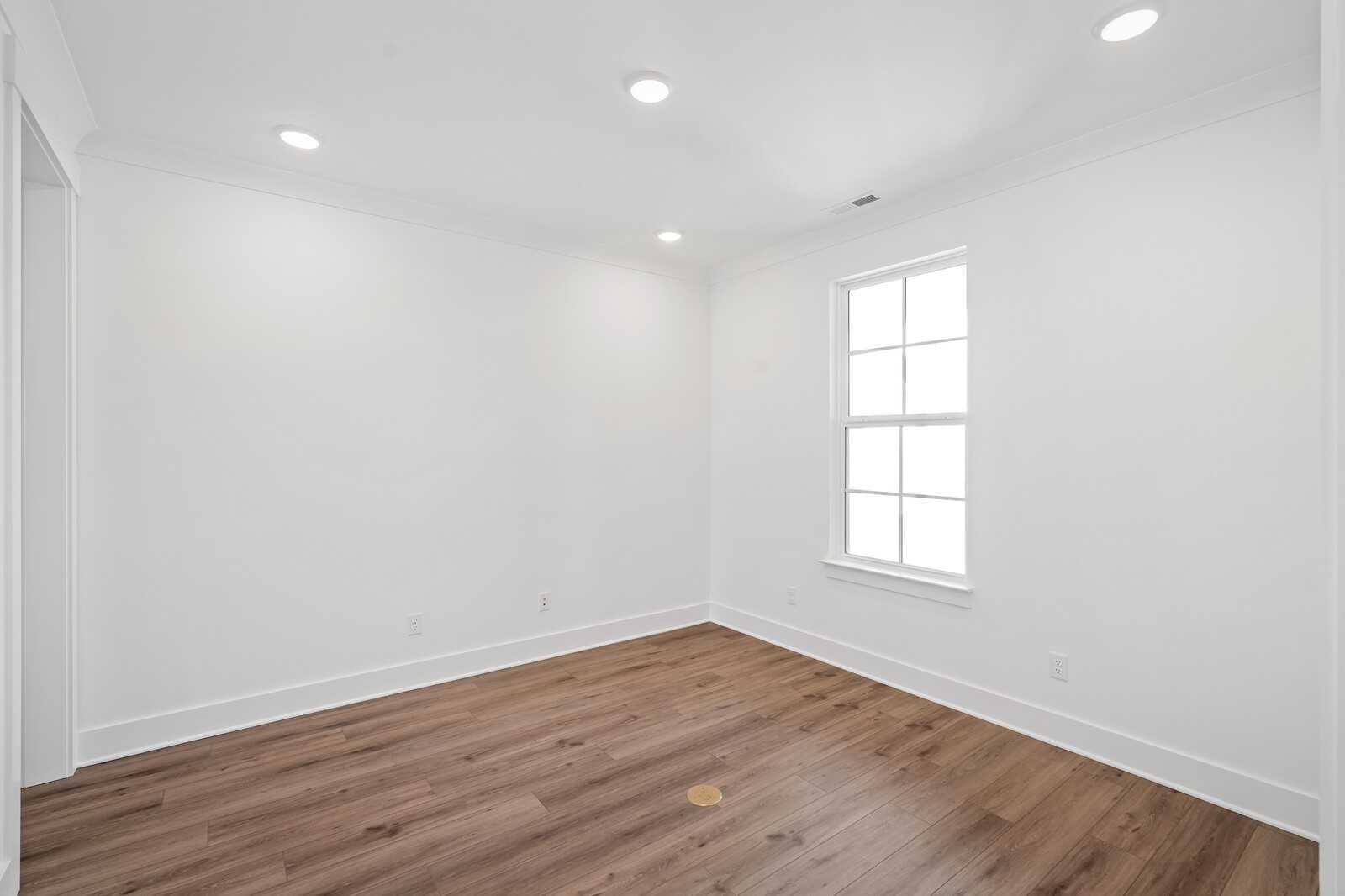 Bright empty bedroom with white walls, hardwood floors, large window, and recessed lighting in Davidson Homes The Hawkins, Murfreesboro, TN