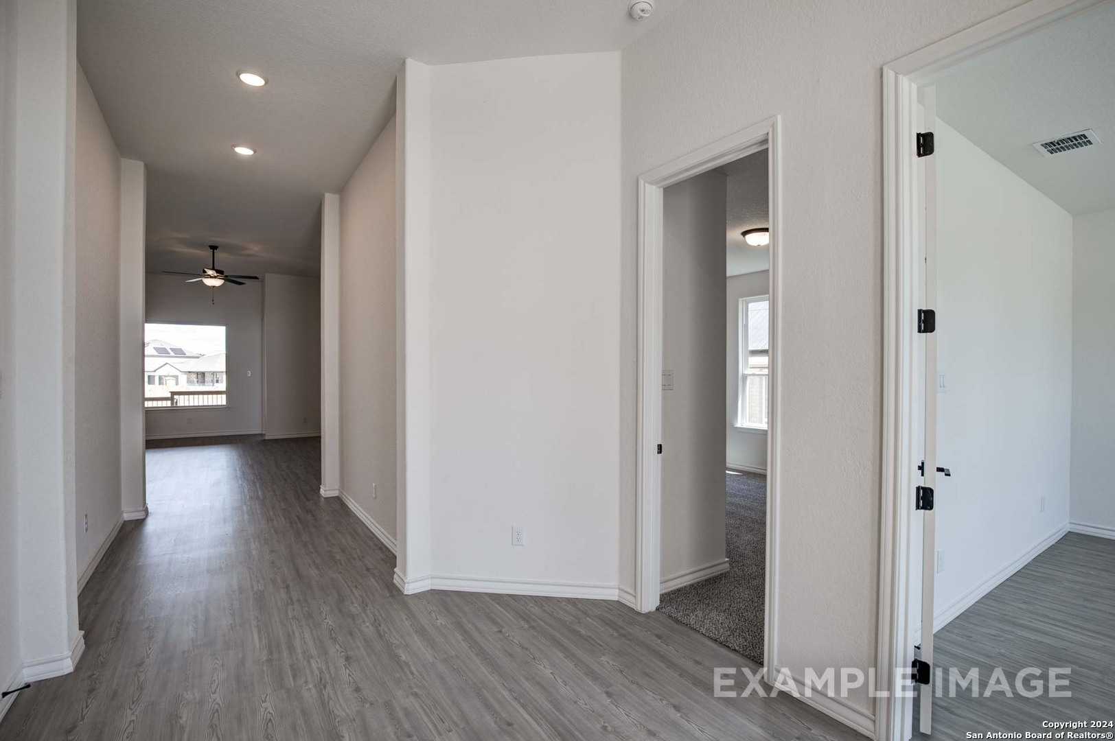 Spacious hallway with white walls, gray luxury vinyl plank floors, ceiling fan, and open doorways in Davidson Homes The Garner C, Castroville TX